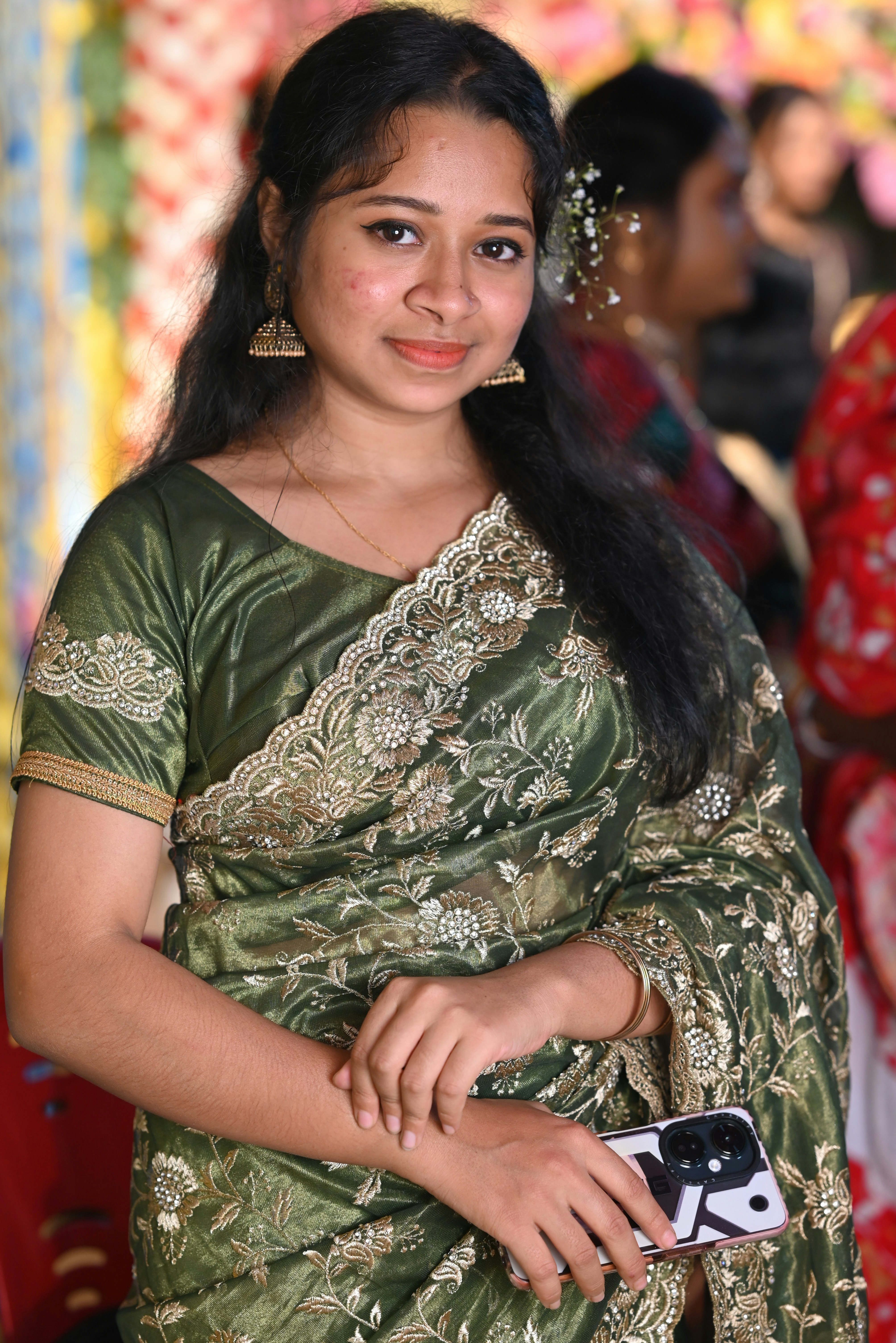 A young woman in a green sari holds a smartphone.