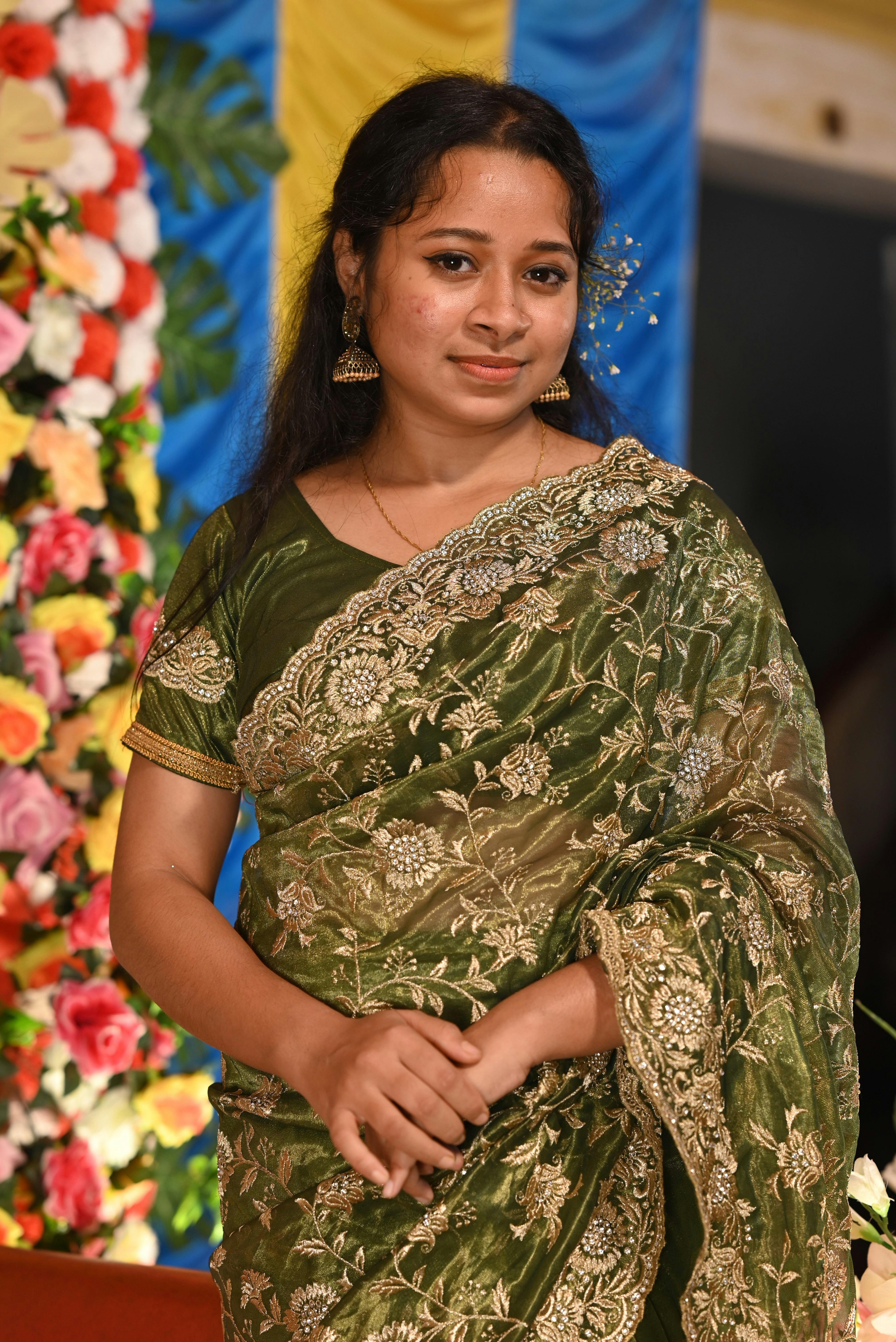A young woman in a green embroidered sari smiles