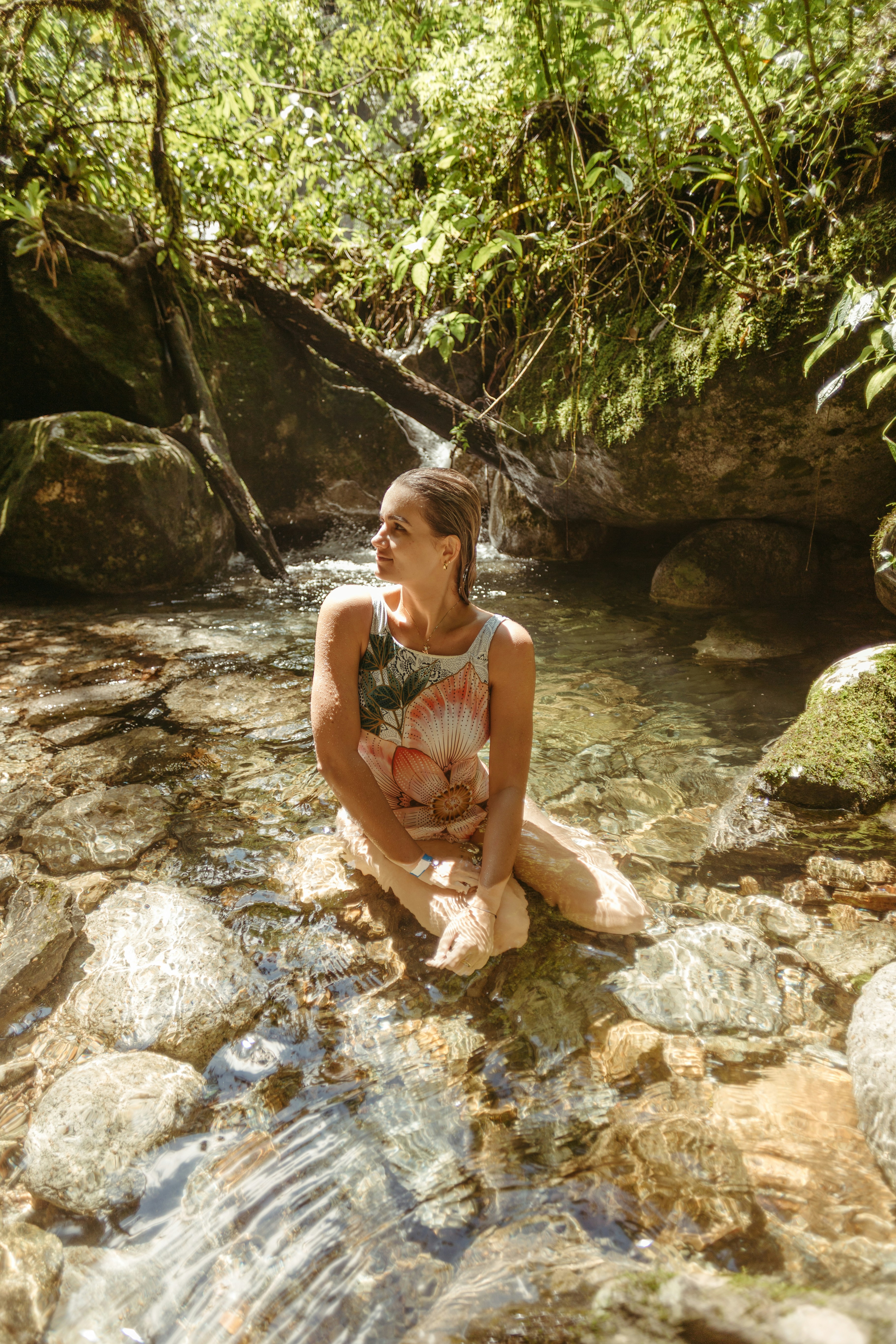 Woman sitting in a shallow stream surrounded by rocks.