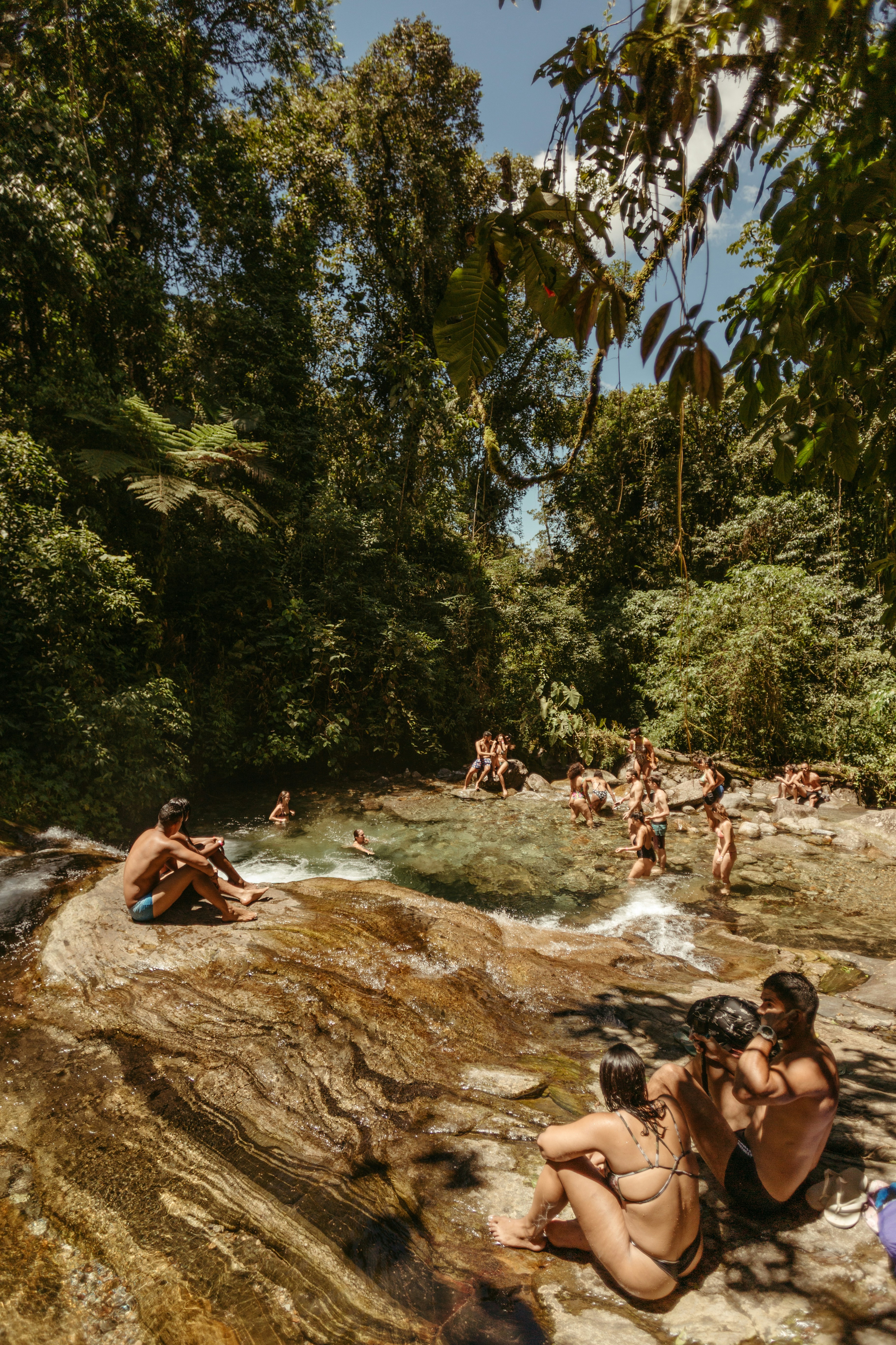 People relaxing by a waterfall in a lush forest.