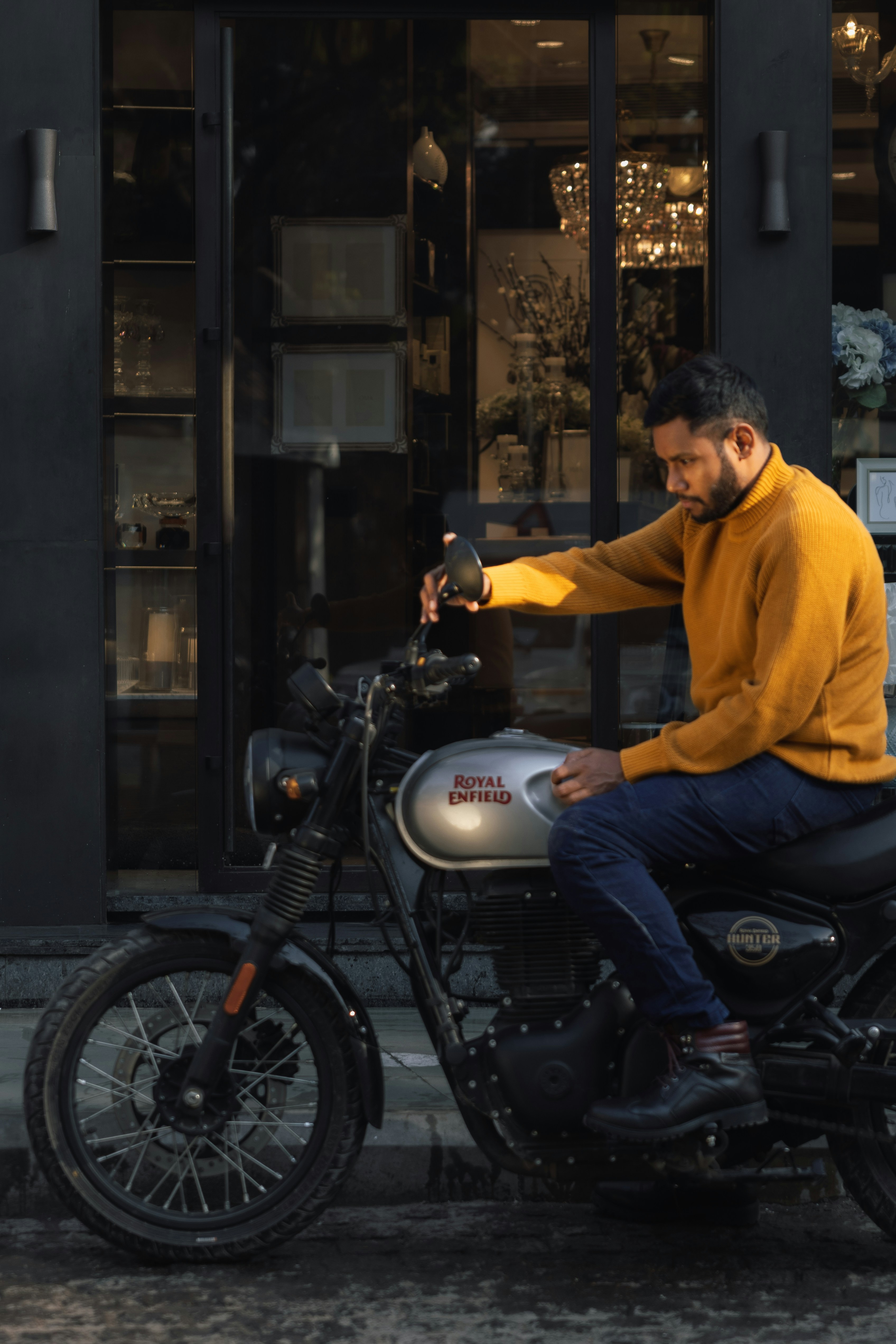 Man in yellow sweater sits on motorcycle outside building