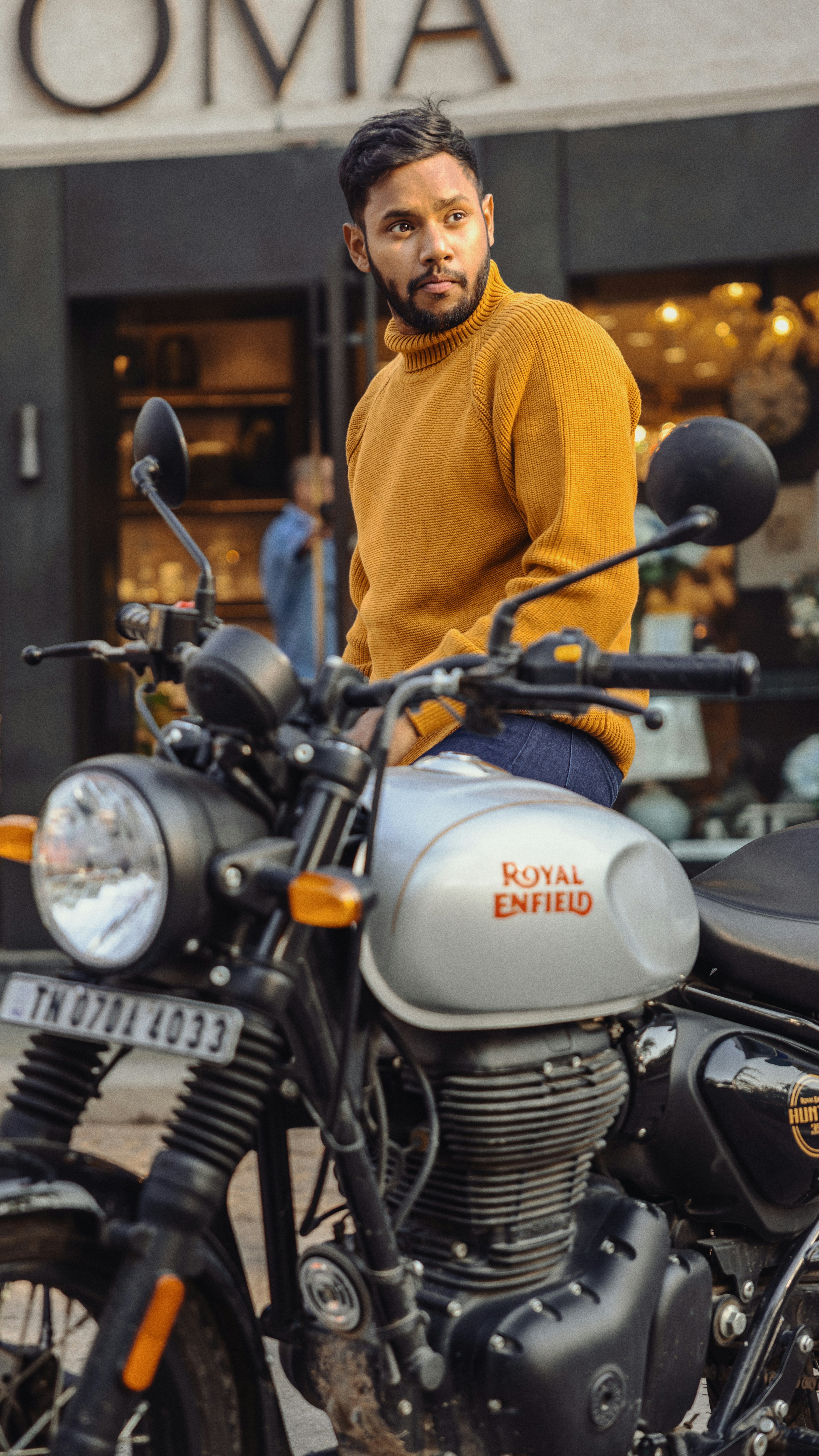 Man in yellow sweater sitting on a royal enfield motorcycle.