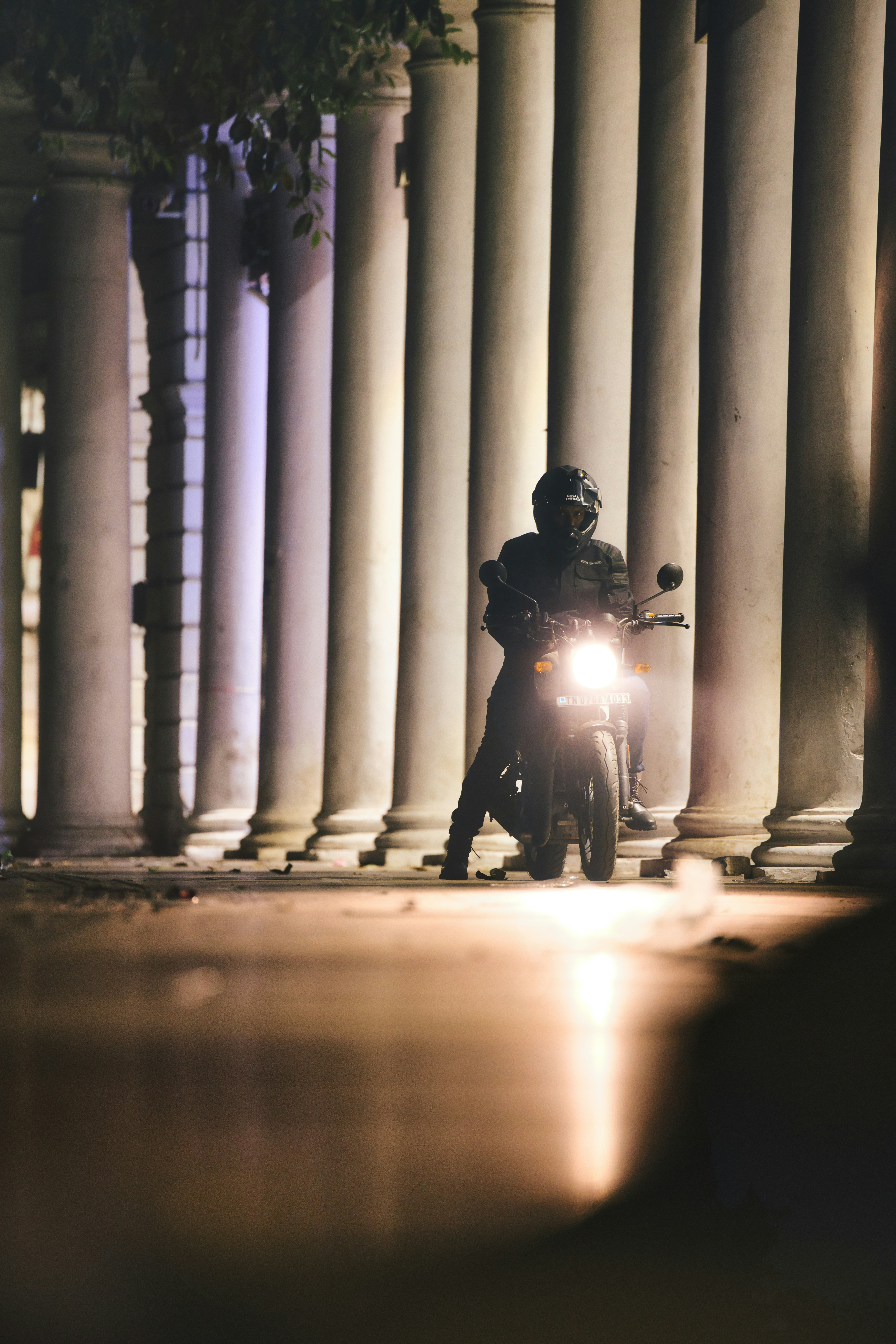 Man in helmet sitting on motorcycle near columns at night