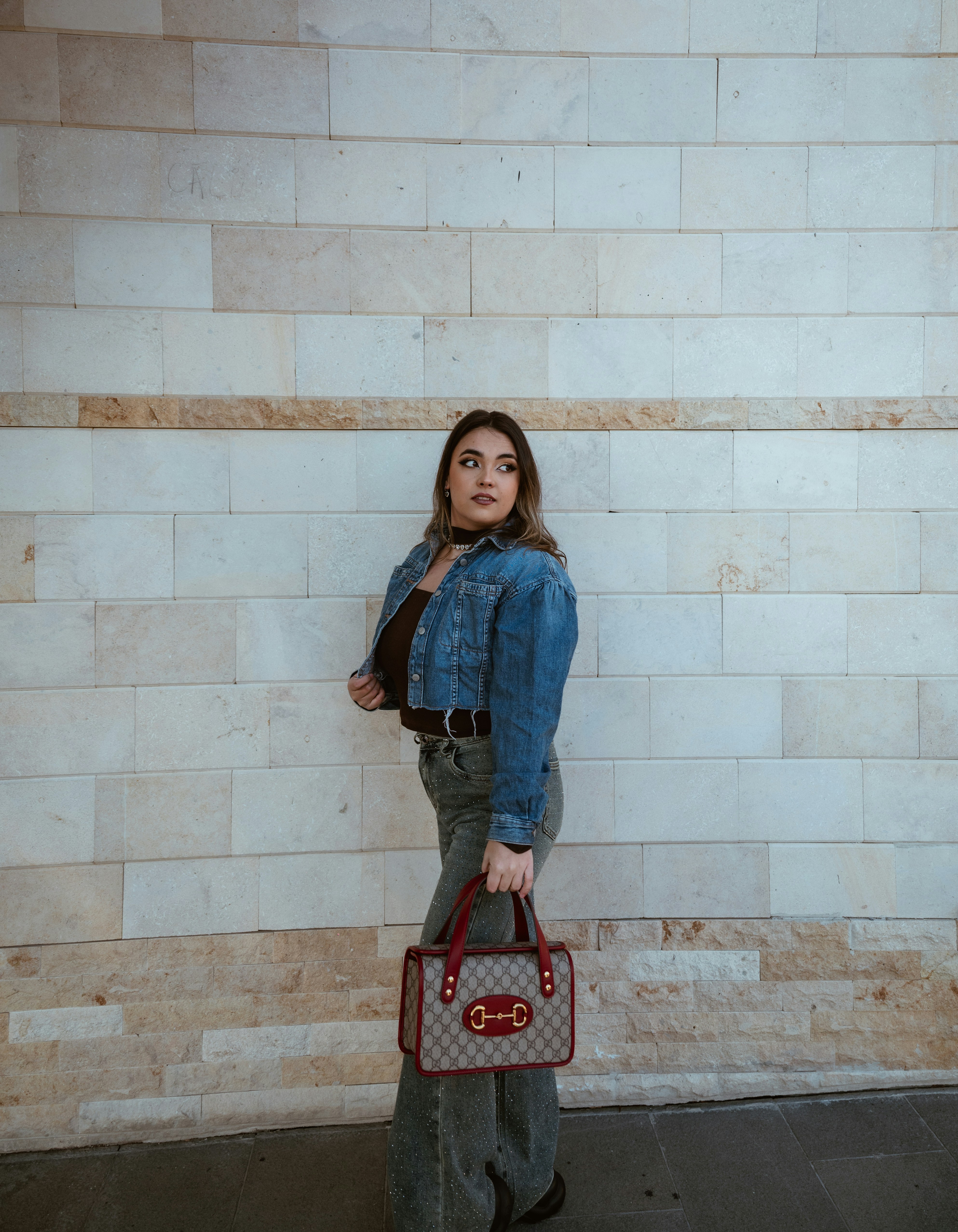 Joven con chaqueta vaquera sosteniendo un bolso de diseñador