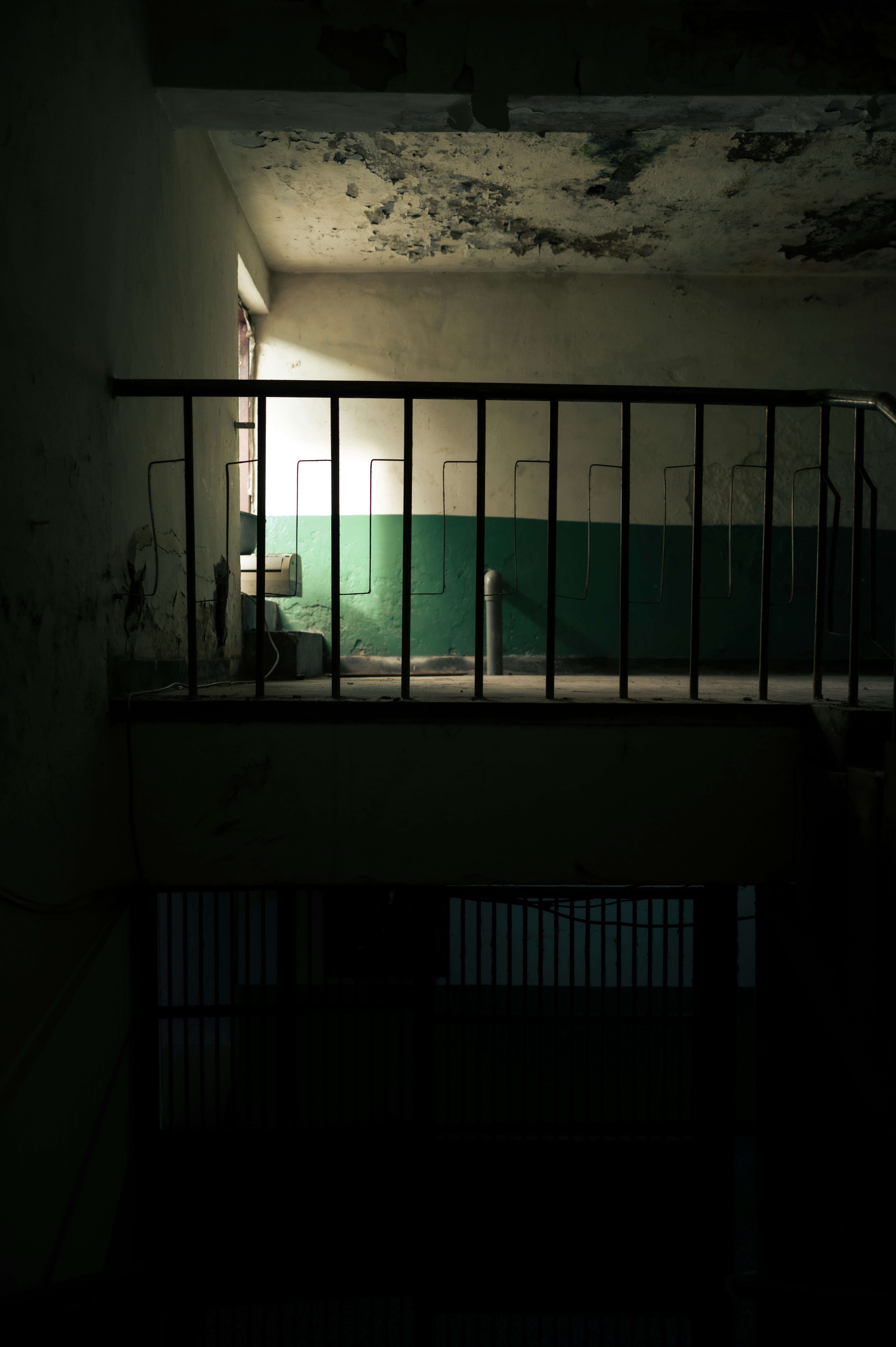 Dimly lit hallway with a metal railing and green wall.