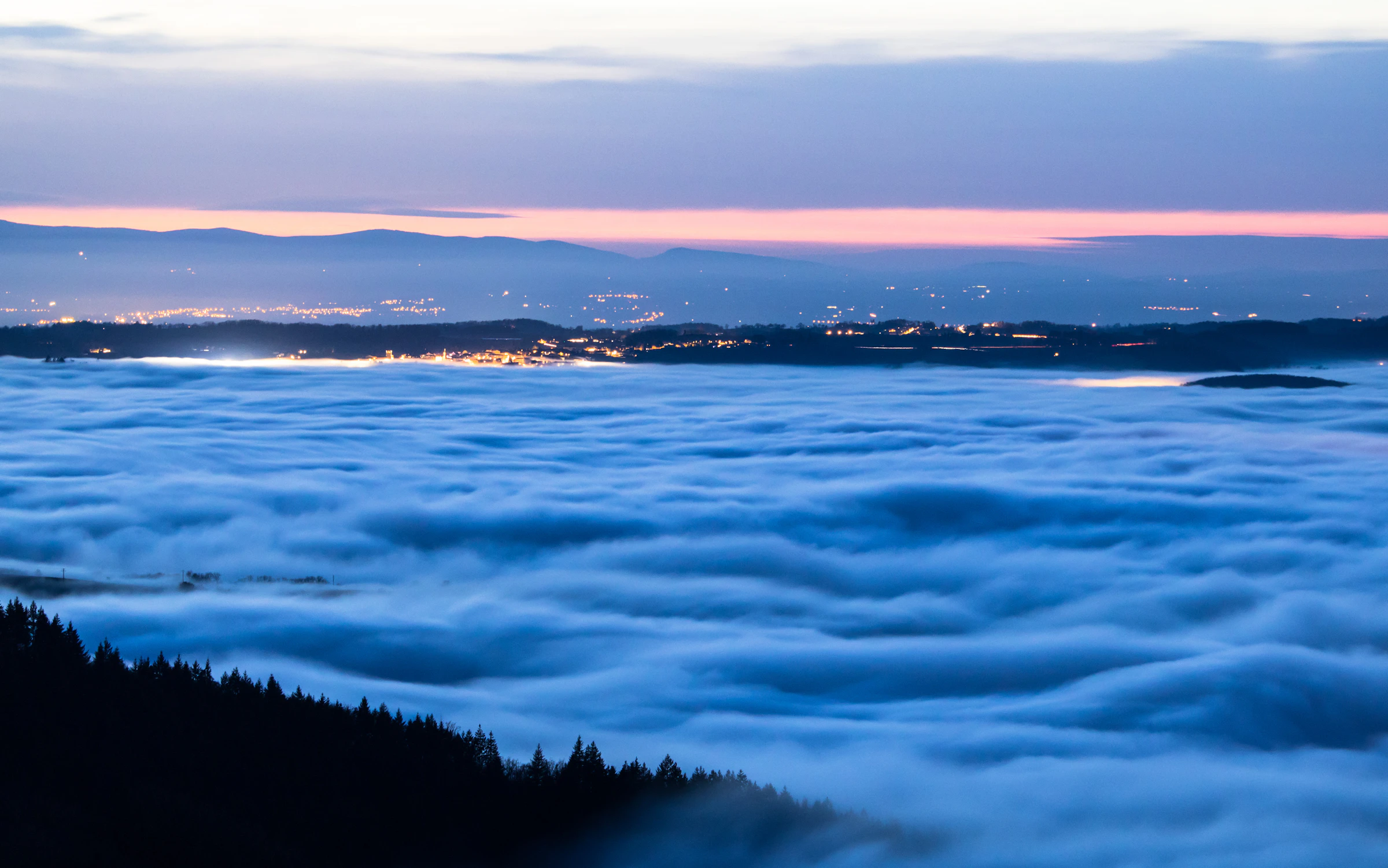 Sea of fog under a dusk sky with distant city lights