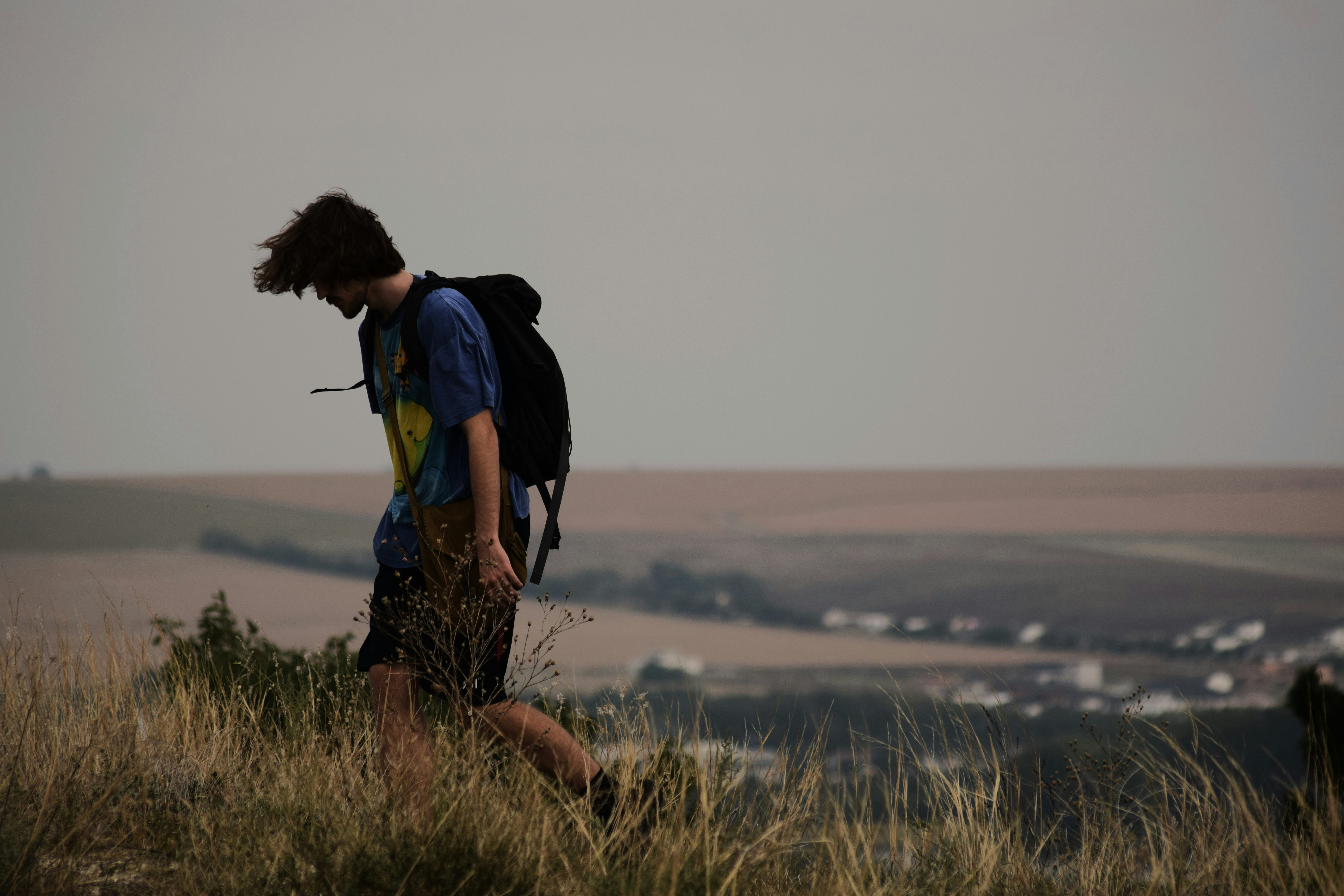 A person with a backpack walks on a grassy hill.