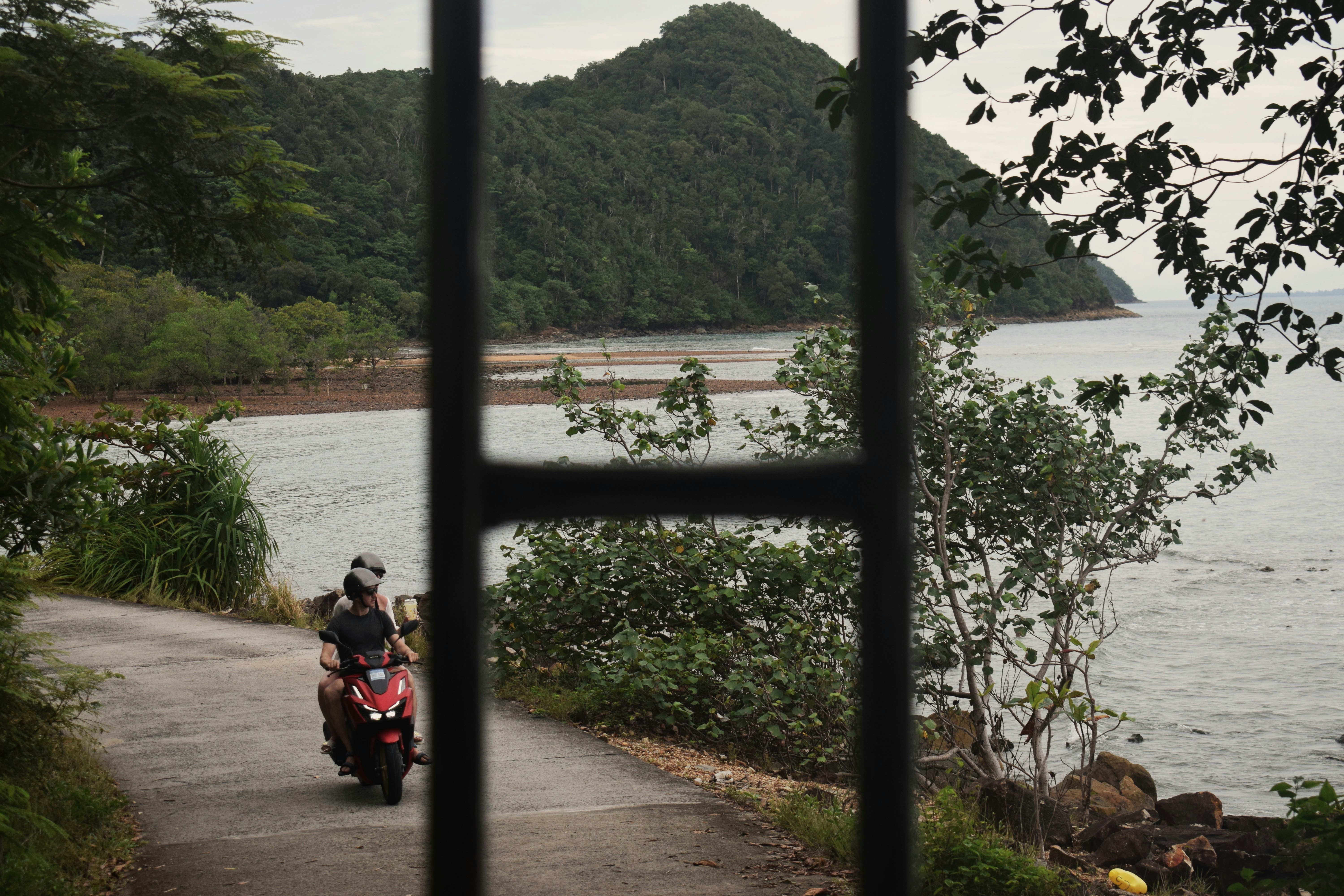 Two people riding a scooter on a coastal road.