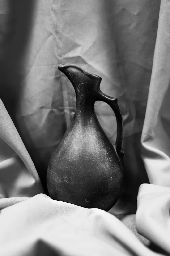 Hand-thrown ceramic pitcher with pulled handle on draped cloth — soft monochrome study