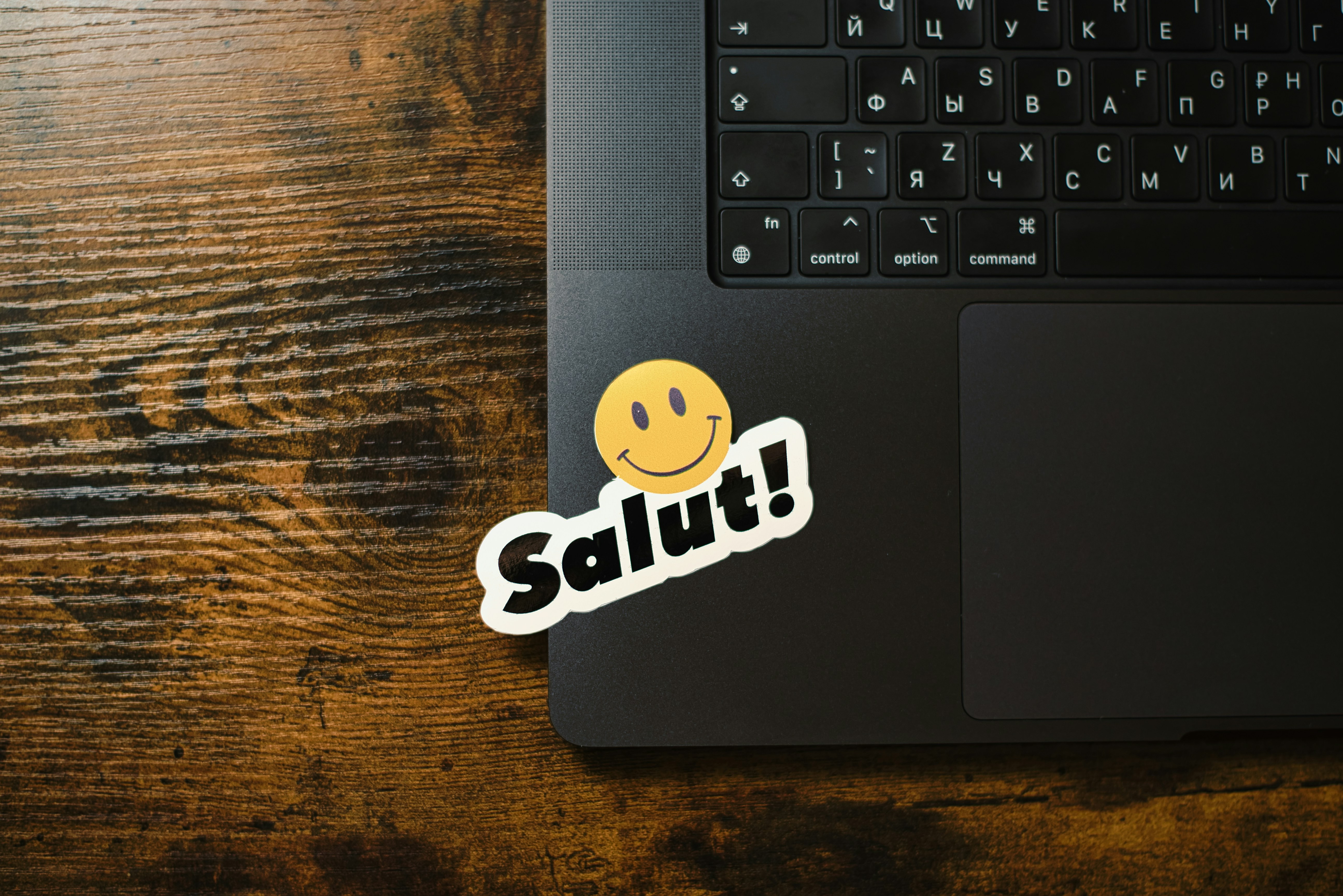 Laptop with a "salut!" smiley sticker on keyboard.