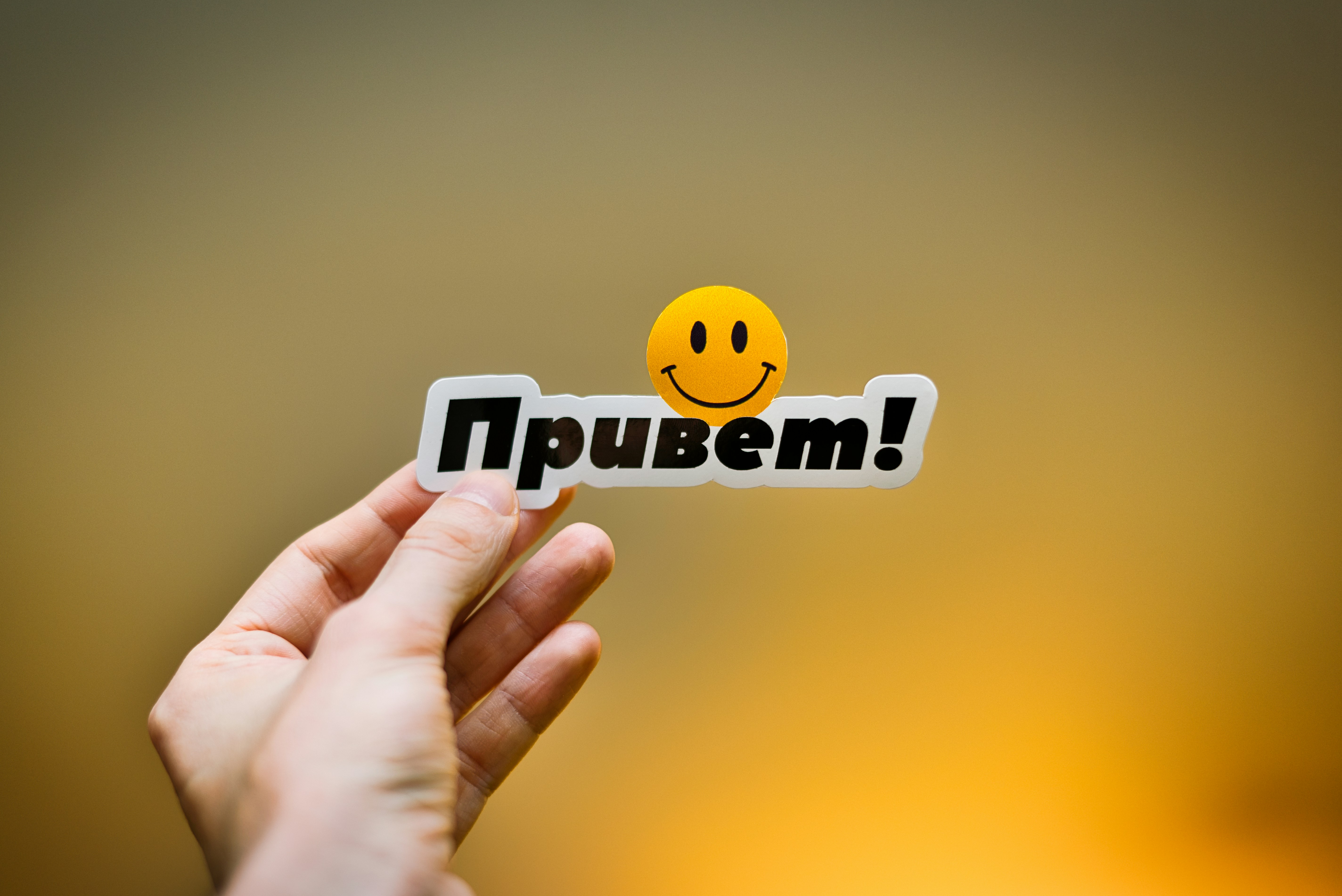 Mano sosteniendo una pegatina con "привет!" y una carita sonriente.