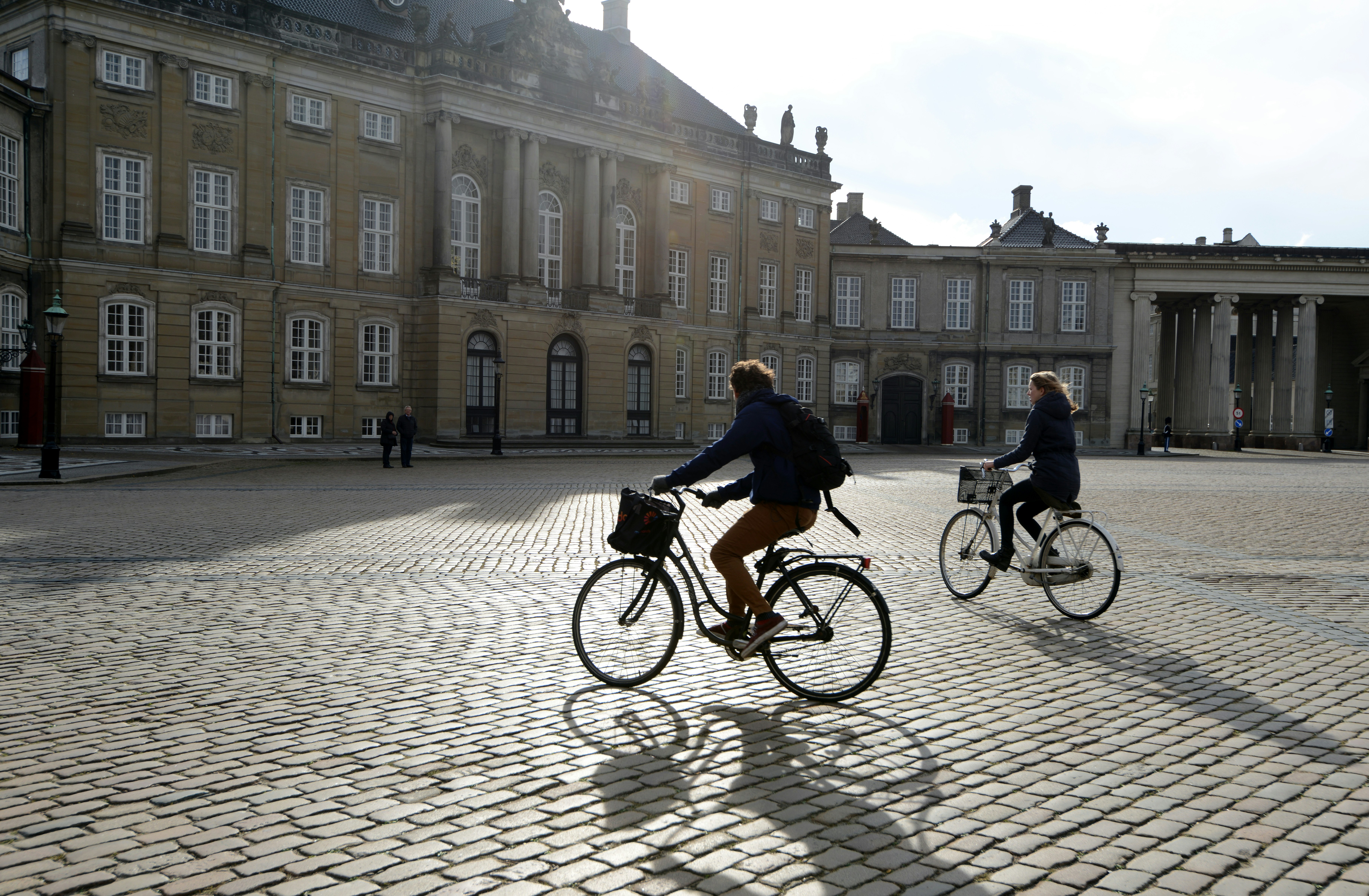 Dos personas en bicicleta en una plaza de adoquines.