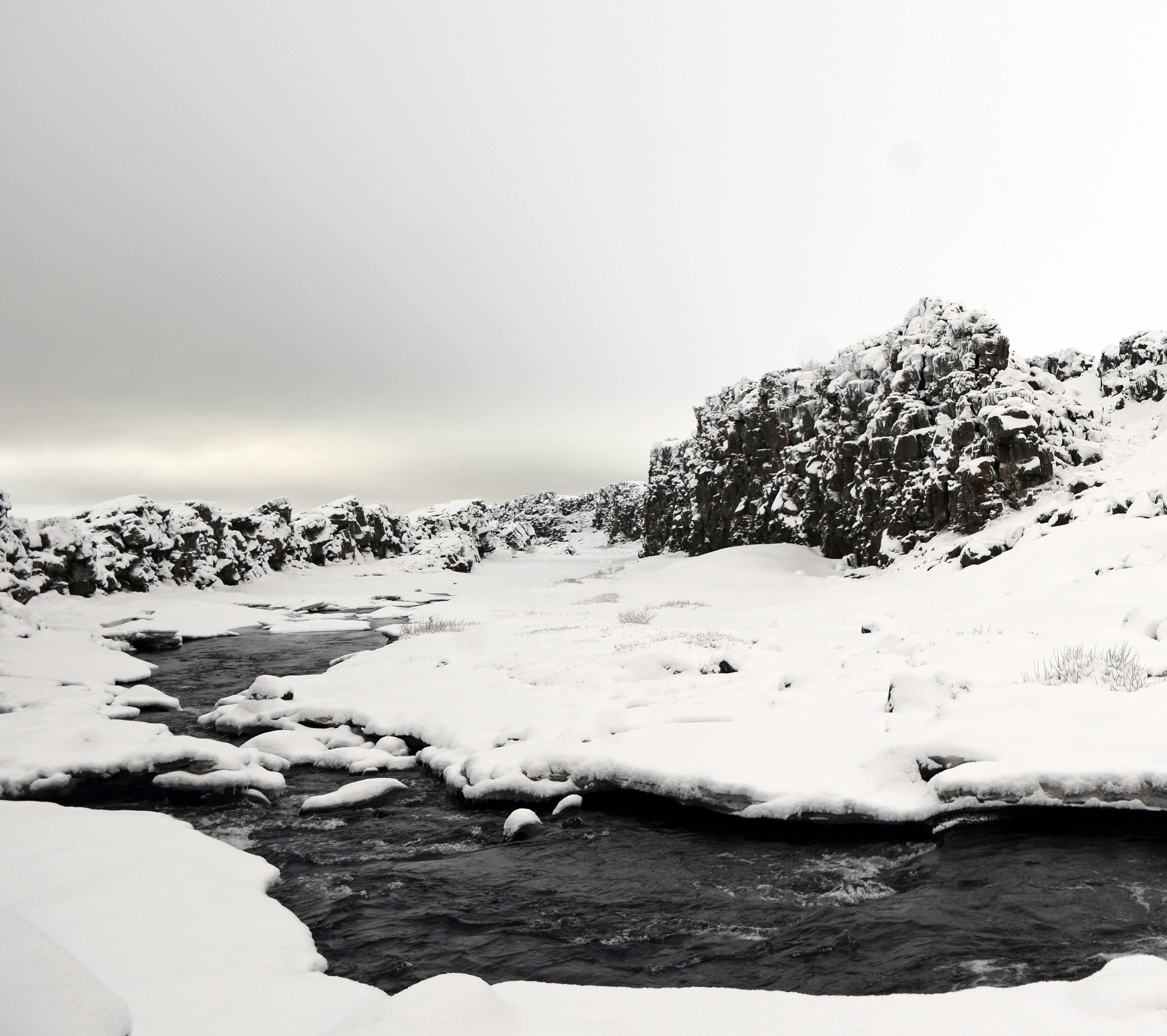 Paisaje nevado con un río y acantilados rocosos.