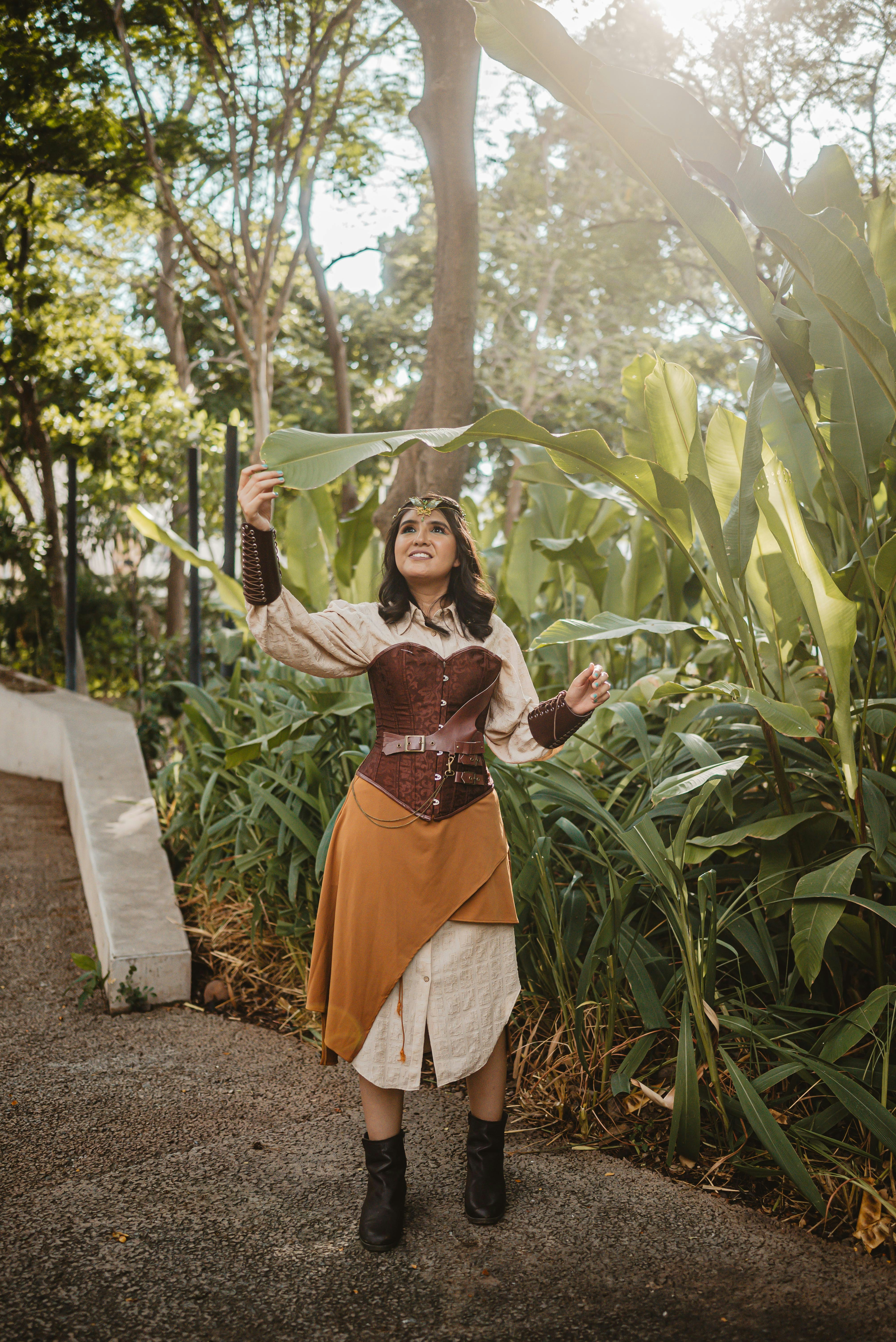 Wanita dengan pakaian steampunk memegang daun hijau besar di luar ruangan.