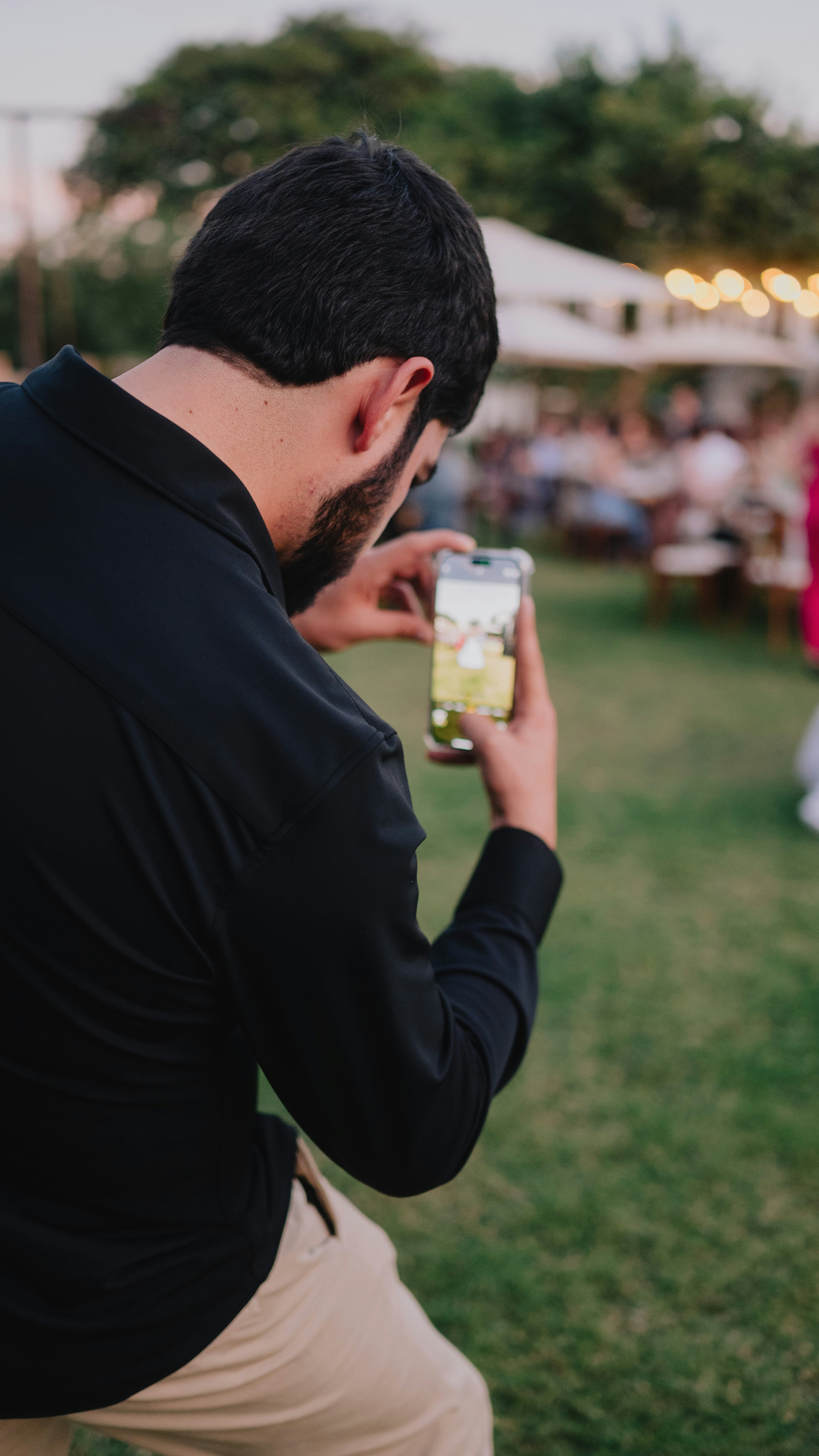 Man filming event with smartphone on grassy field.