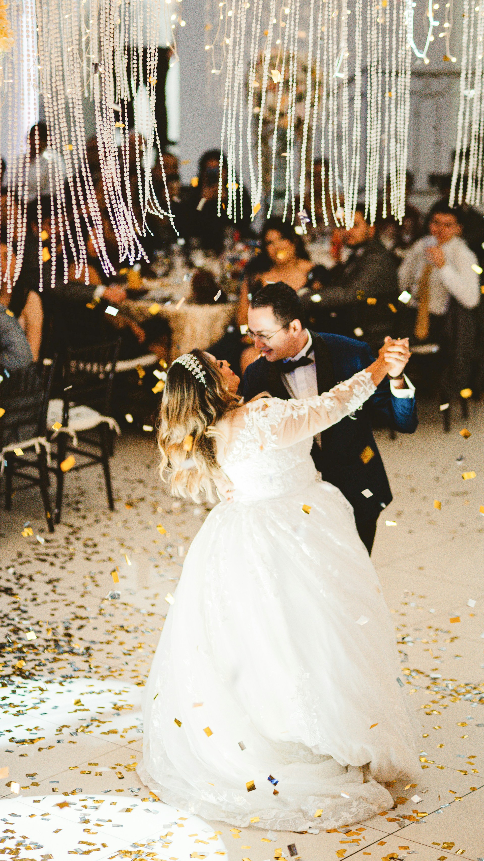 Newlyweds dance surrounded by falling confetti and lights.