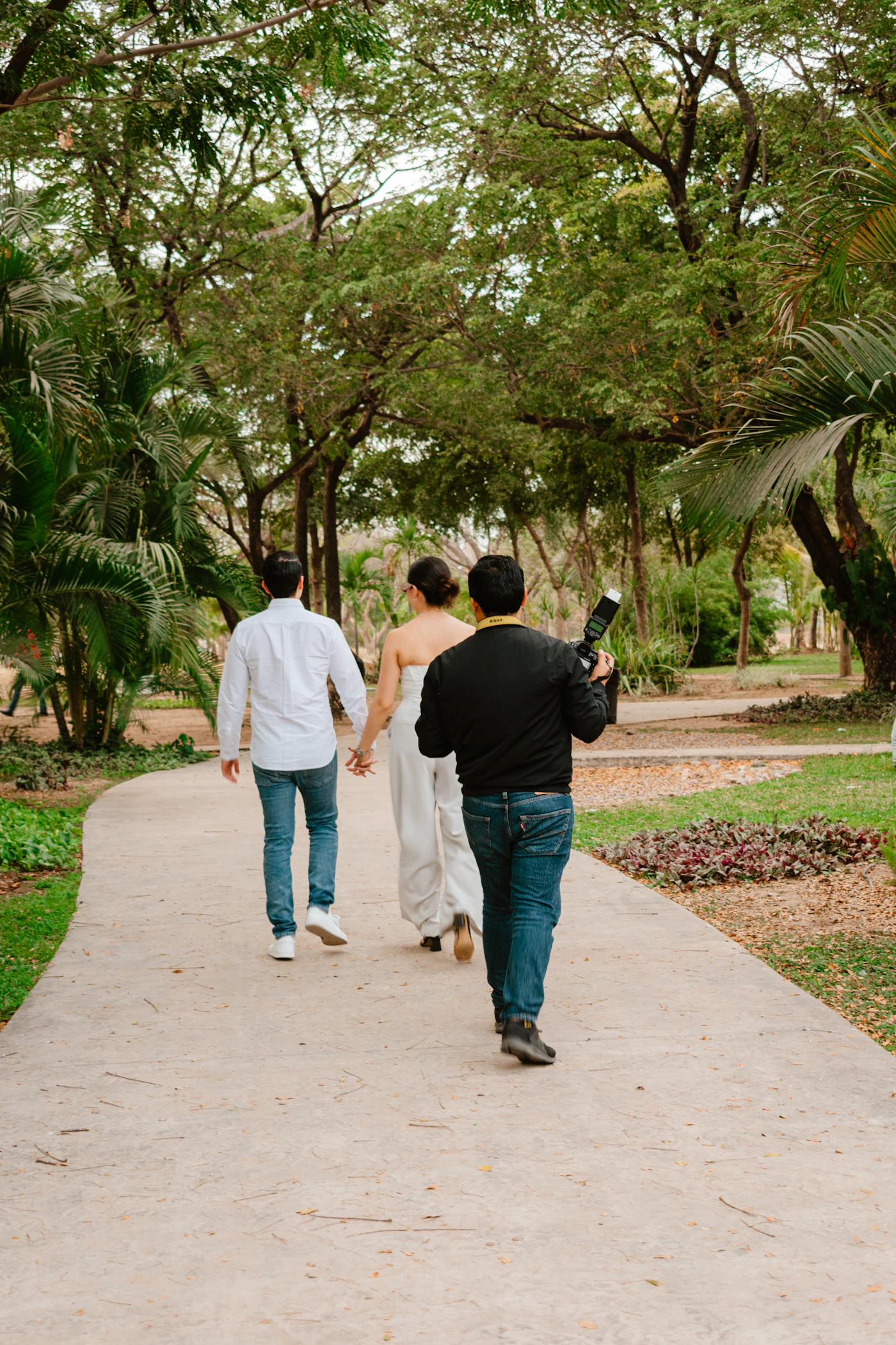 Wedding photographer visible in the frame shooting from behind as a couple walks away from the camera in a natural outdoor setting