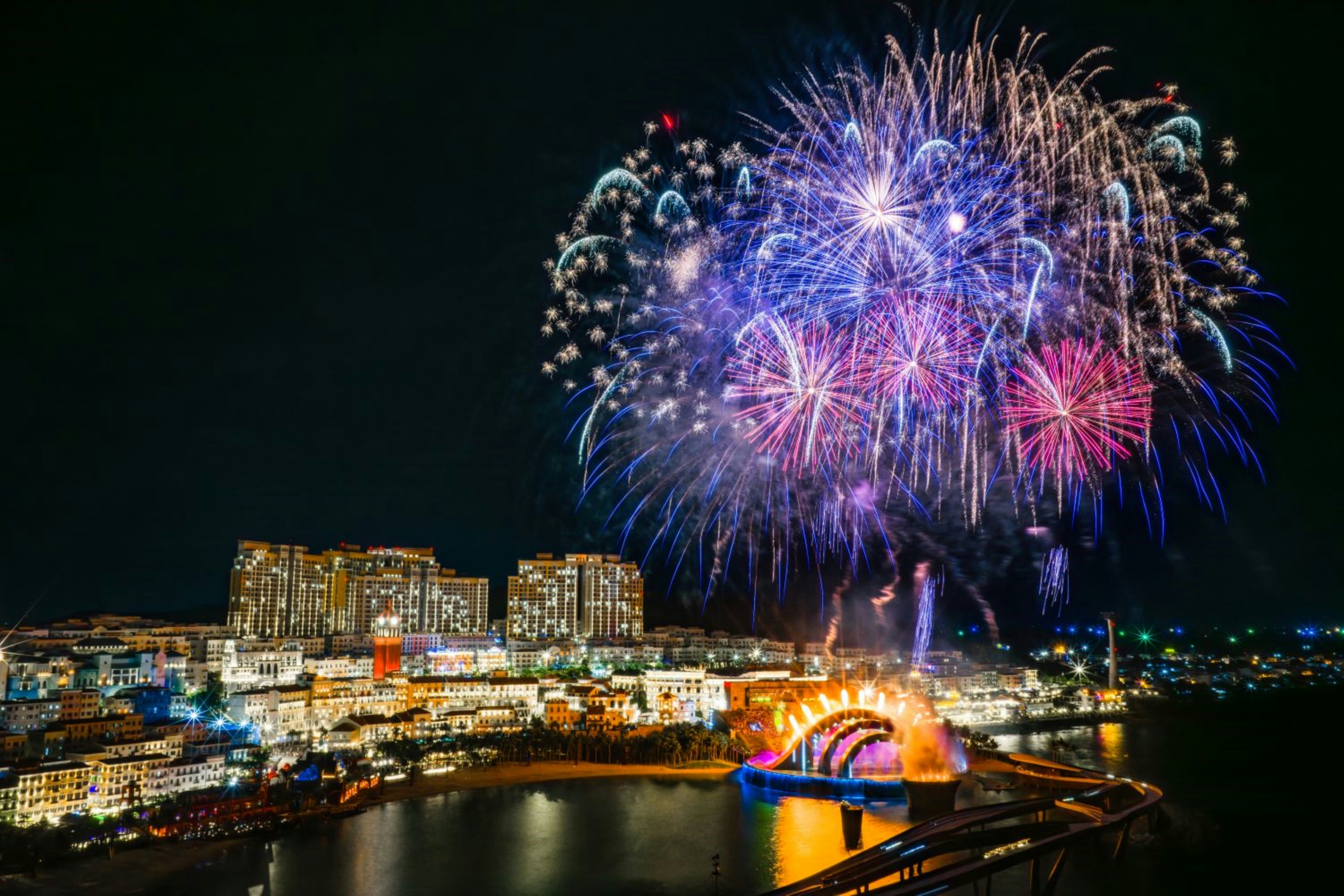 Fireworks explode over a city skyline at night.