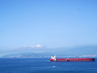 Red cargo ship sailing on a clear blue sea.