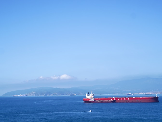 Red cargo ship sailing on a clear blue sea.