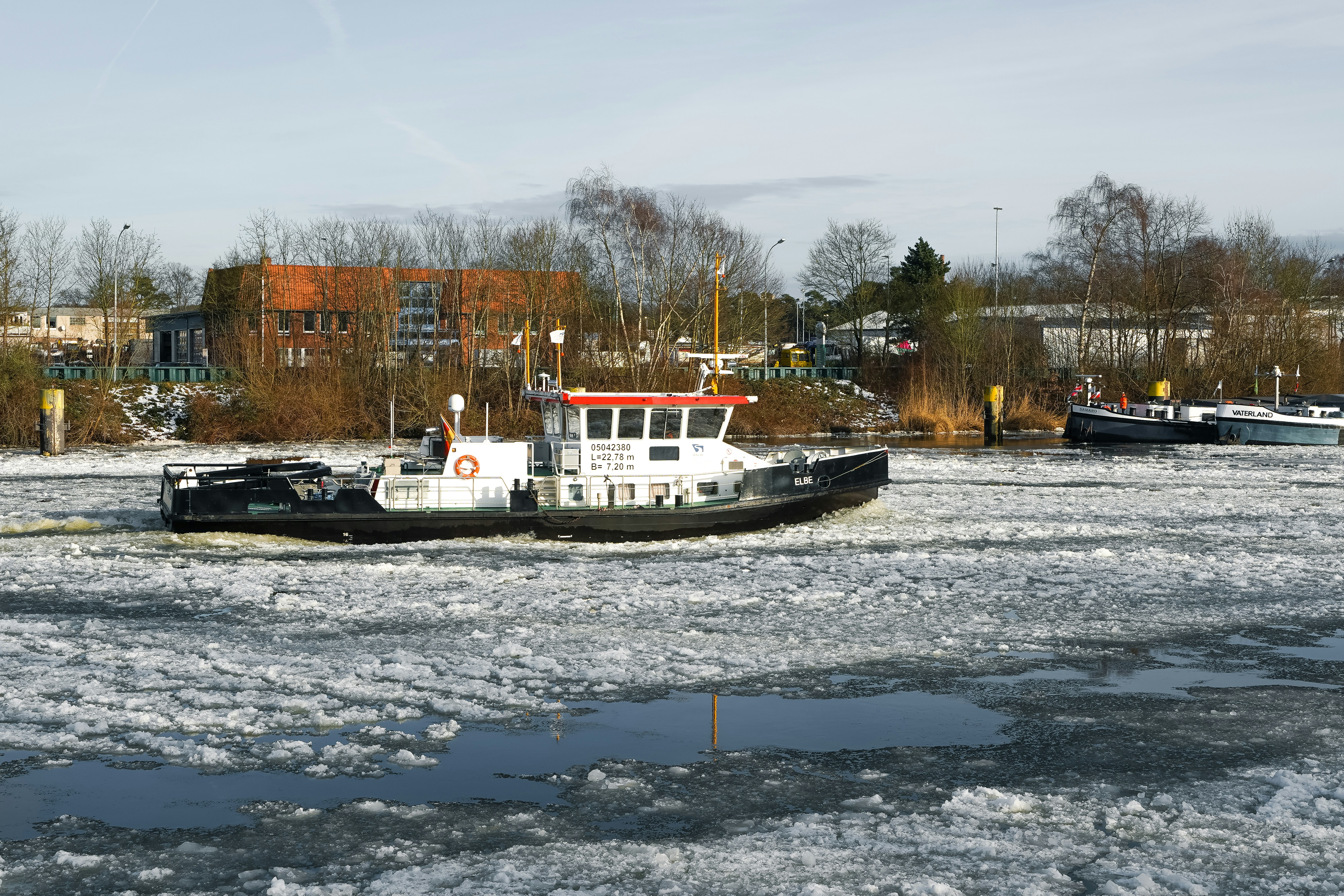 A tugboat navigates through icy water near a shore.