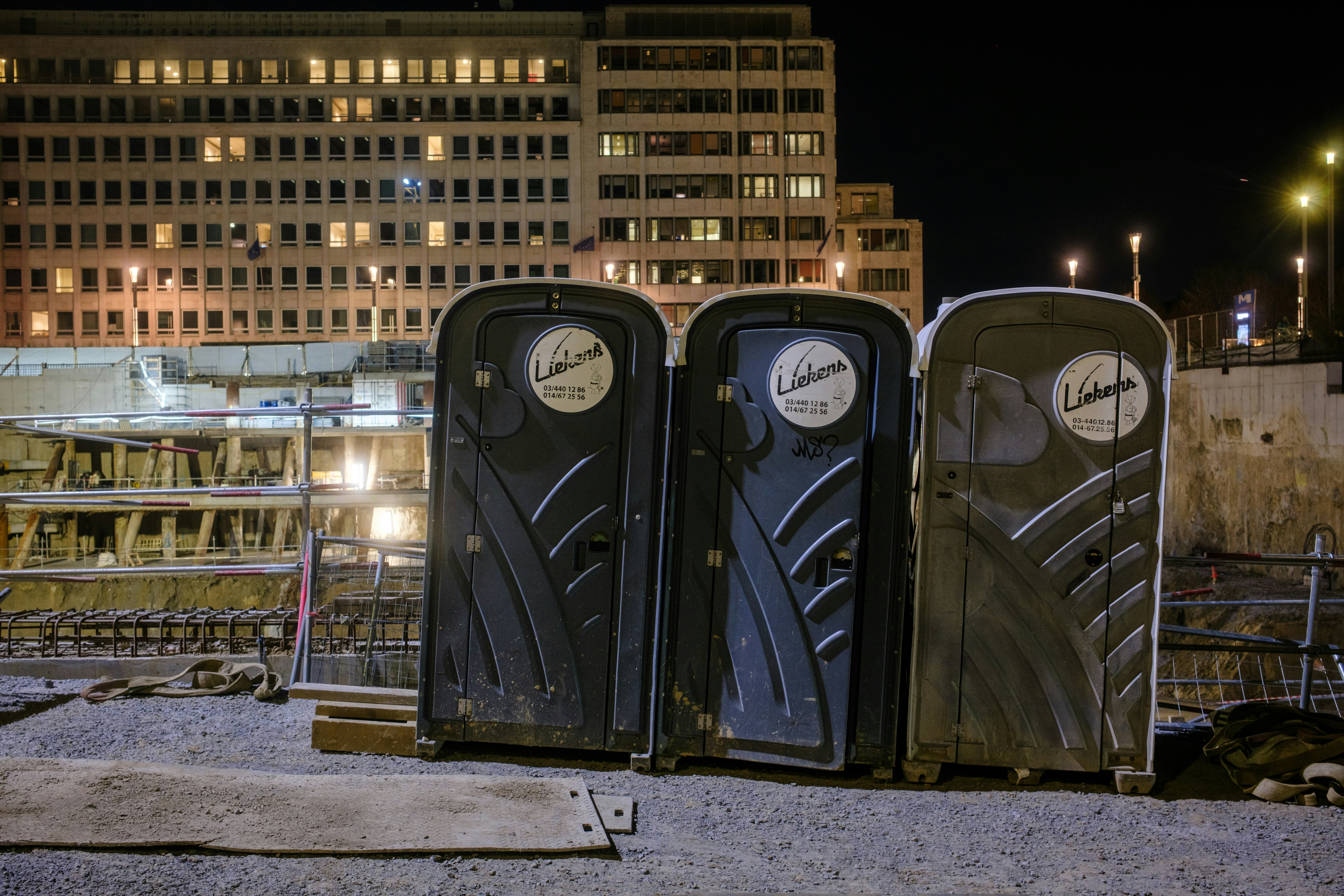 Three portable toilets stand outside a building at night