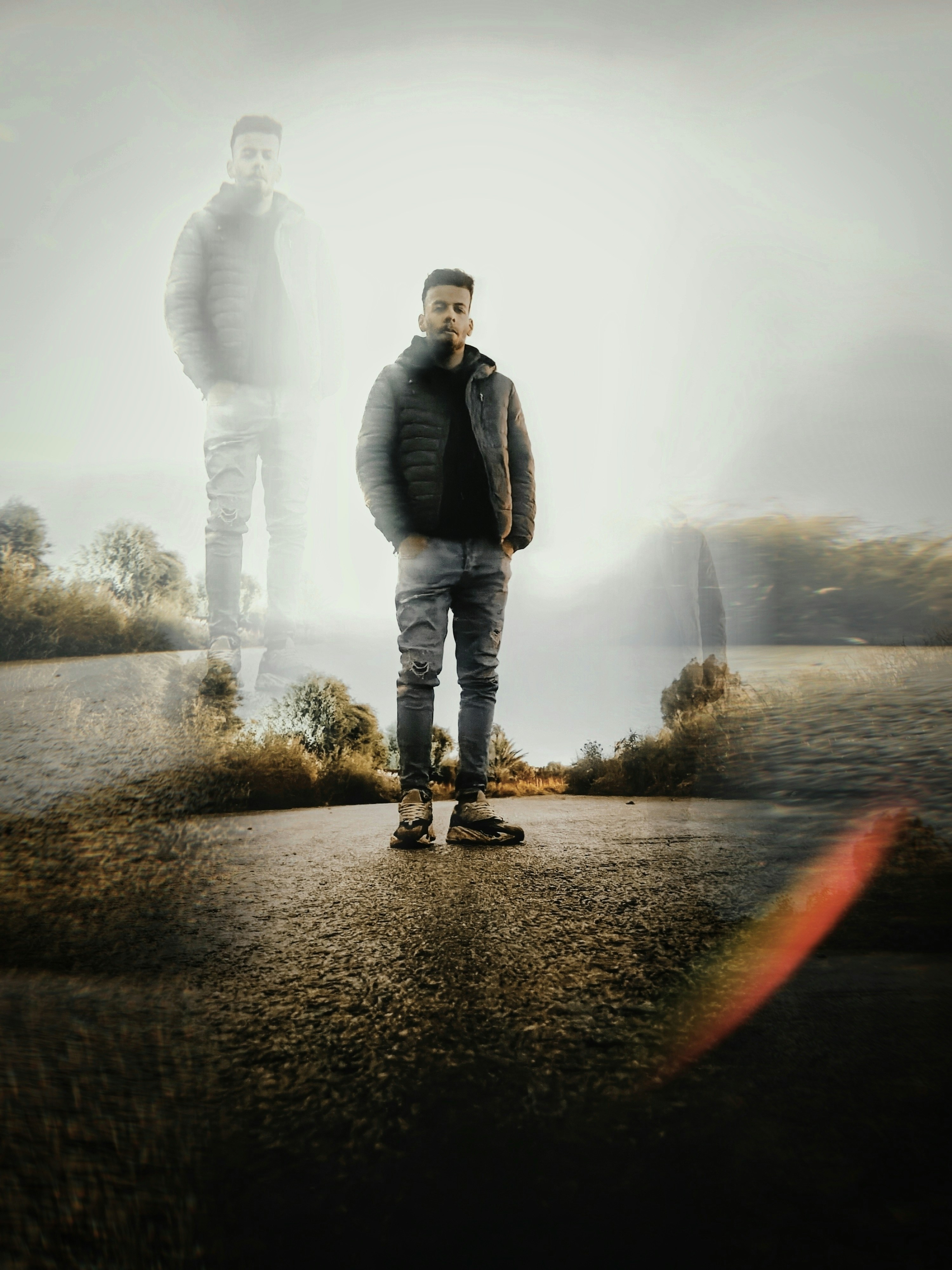 A man stands in a landscape with a ghostly double.