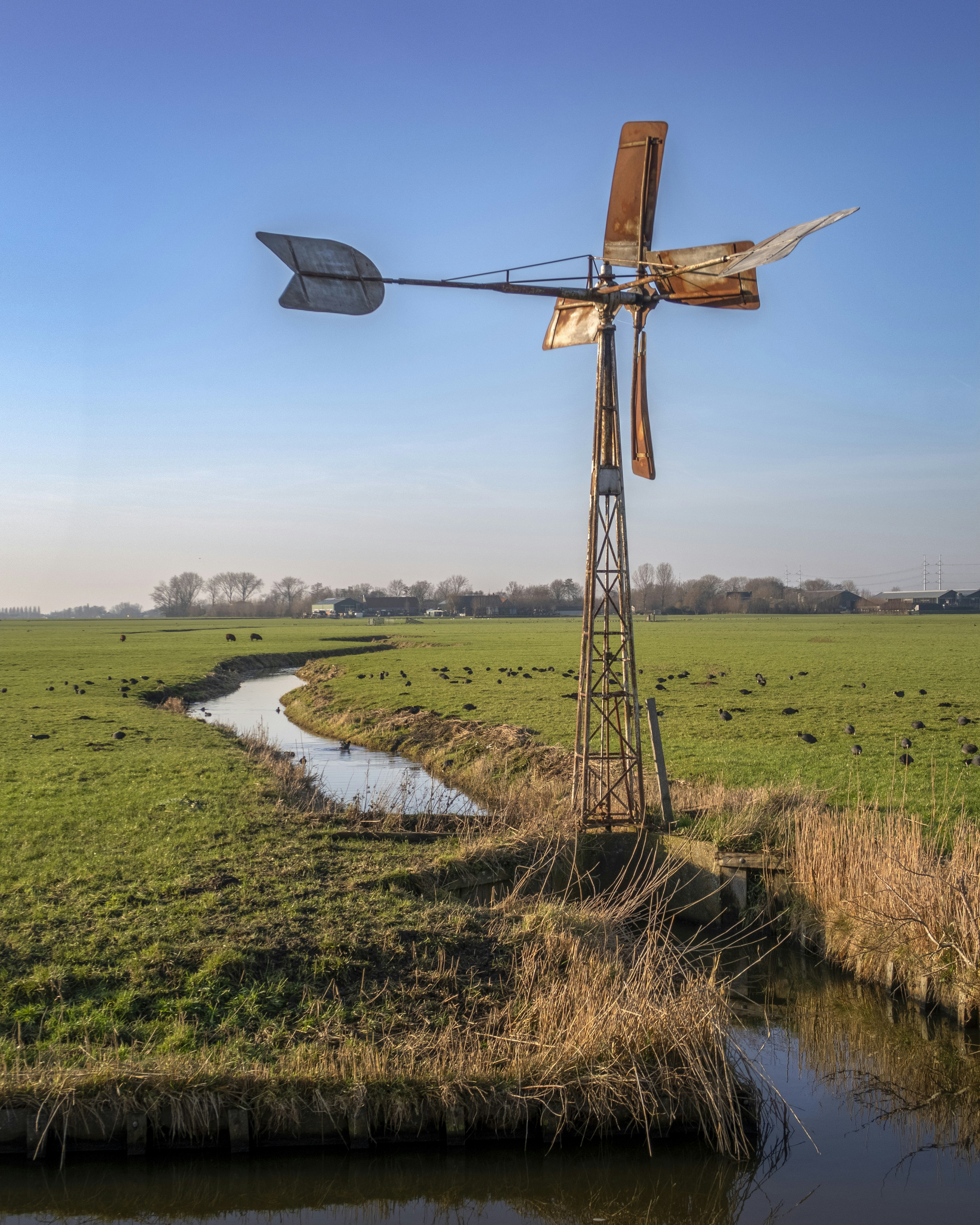 Old windmill stands in a green field by a stream.