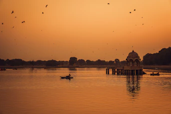 Boats on a lake with a domed structure at sunset.
