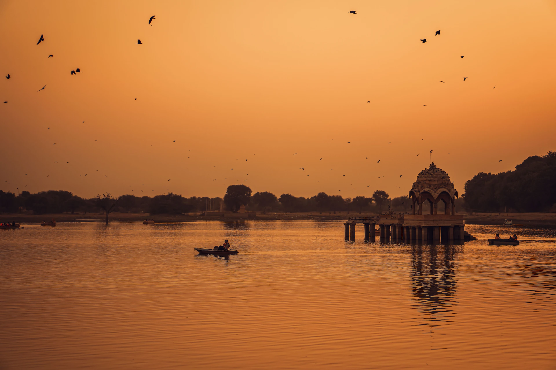 Boats on a lake with a domed structure at sunset.