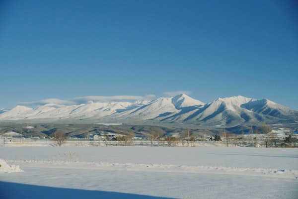 A line of snow-covered mountains, the Tokachi range, rising above flat white farmland under a pale winter sky