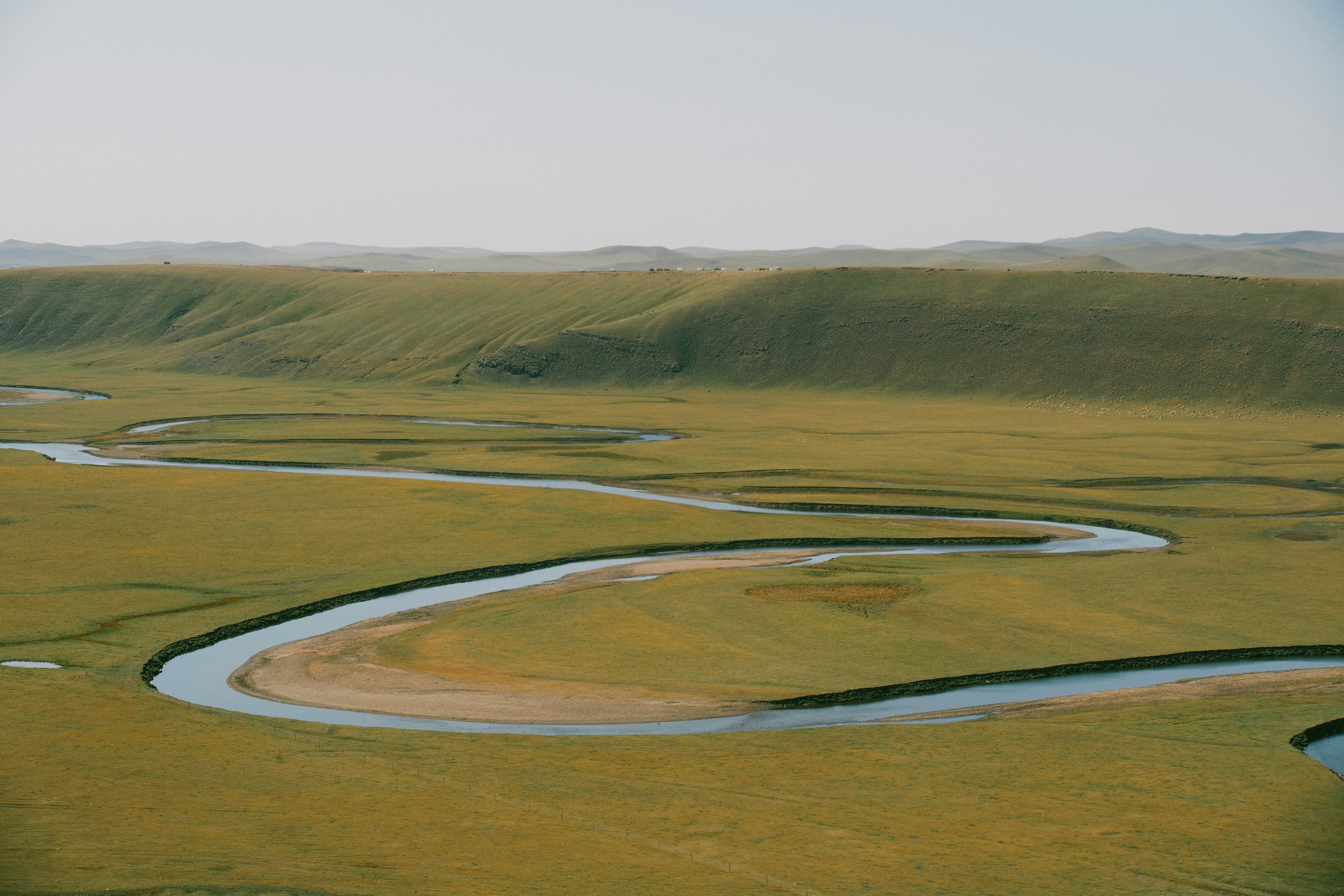 A winding river flows through a vast, grassy plain.