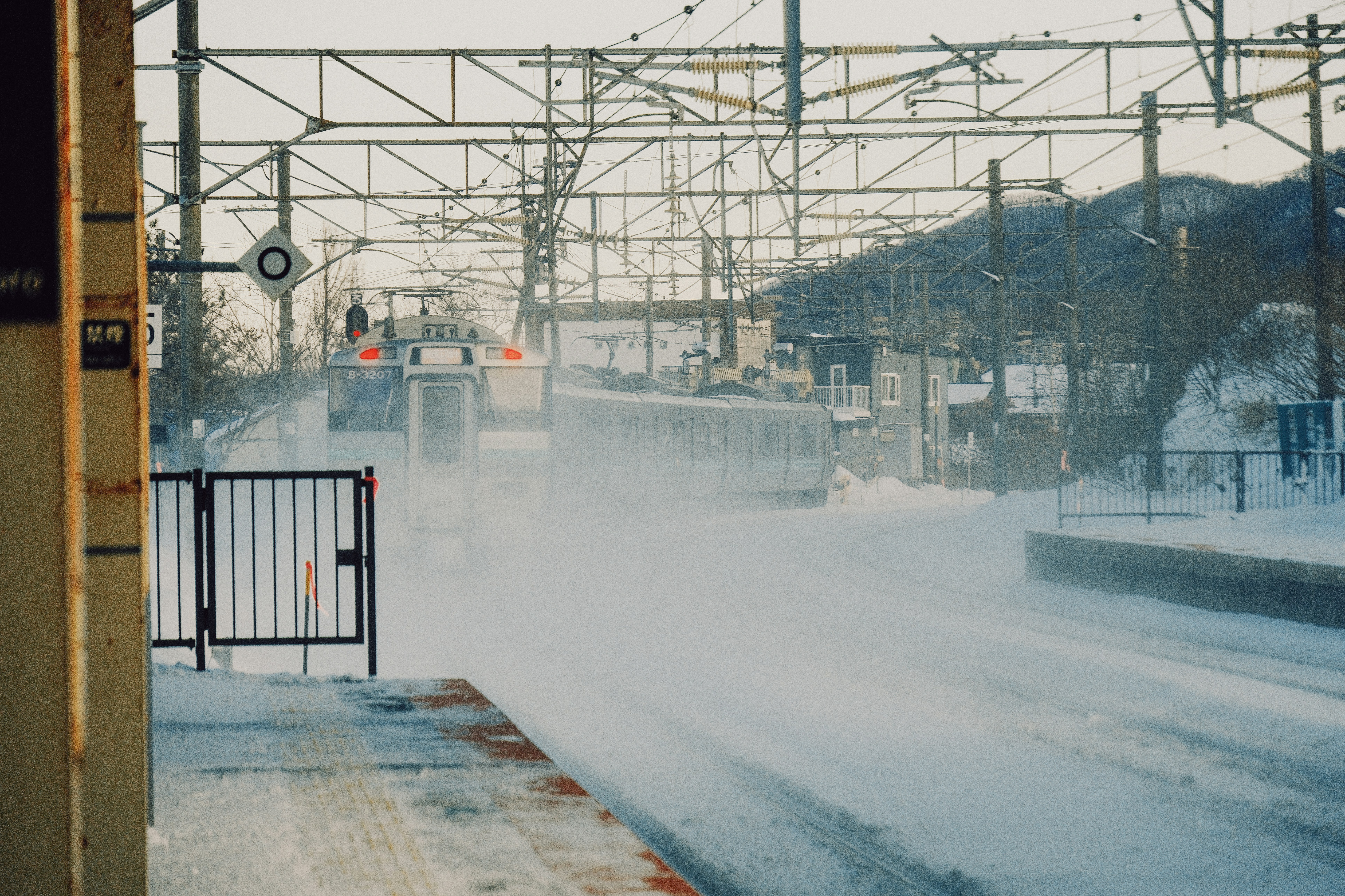 Snowy train station with blowing snow and tracks.