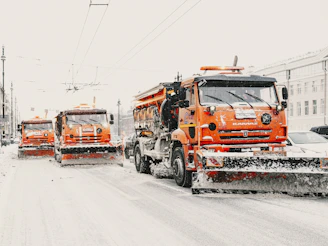 Three orange snow plows clearing a snowy street