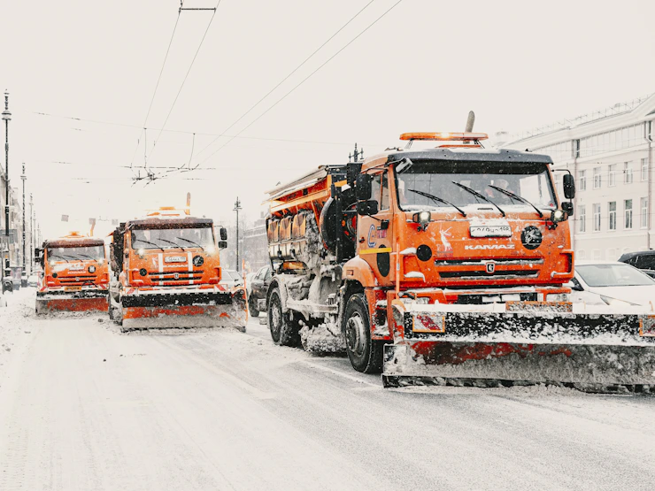 Three orange snow plows clearing a snowy street