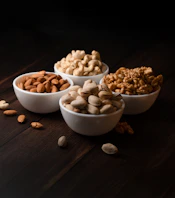 Four bowls of assorted nuts on a dark surface.