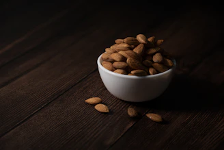 A white bowl filled with almonds on a wooden surface.