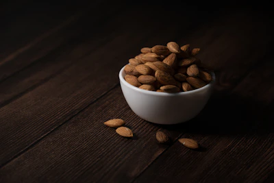 A white bowl filled with almonds on a wooden surface.