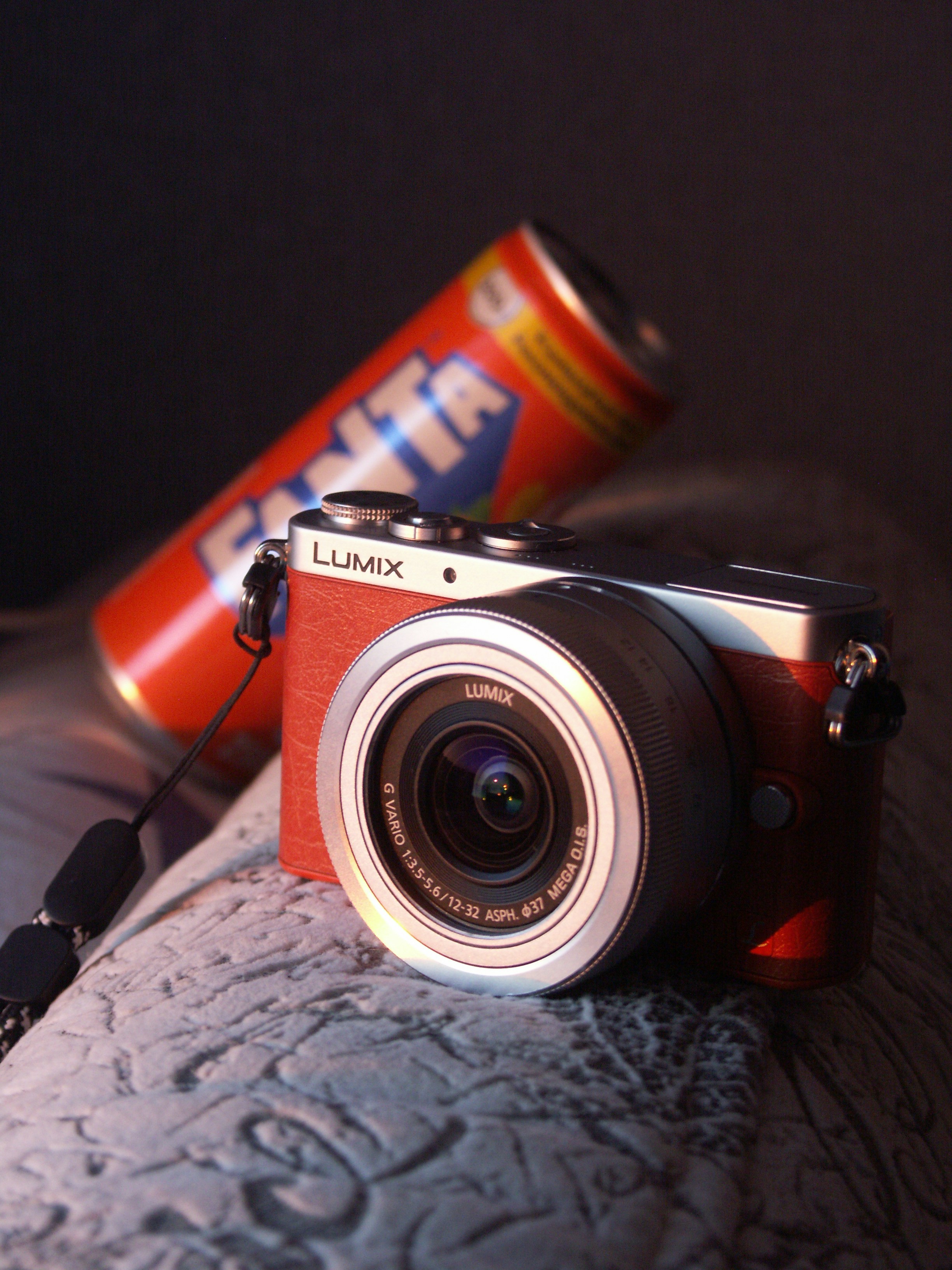 A red lumix camera rests beside a fanta can.