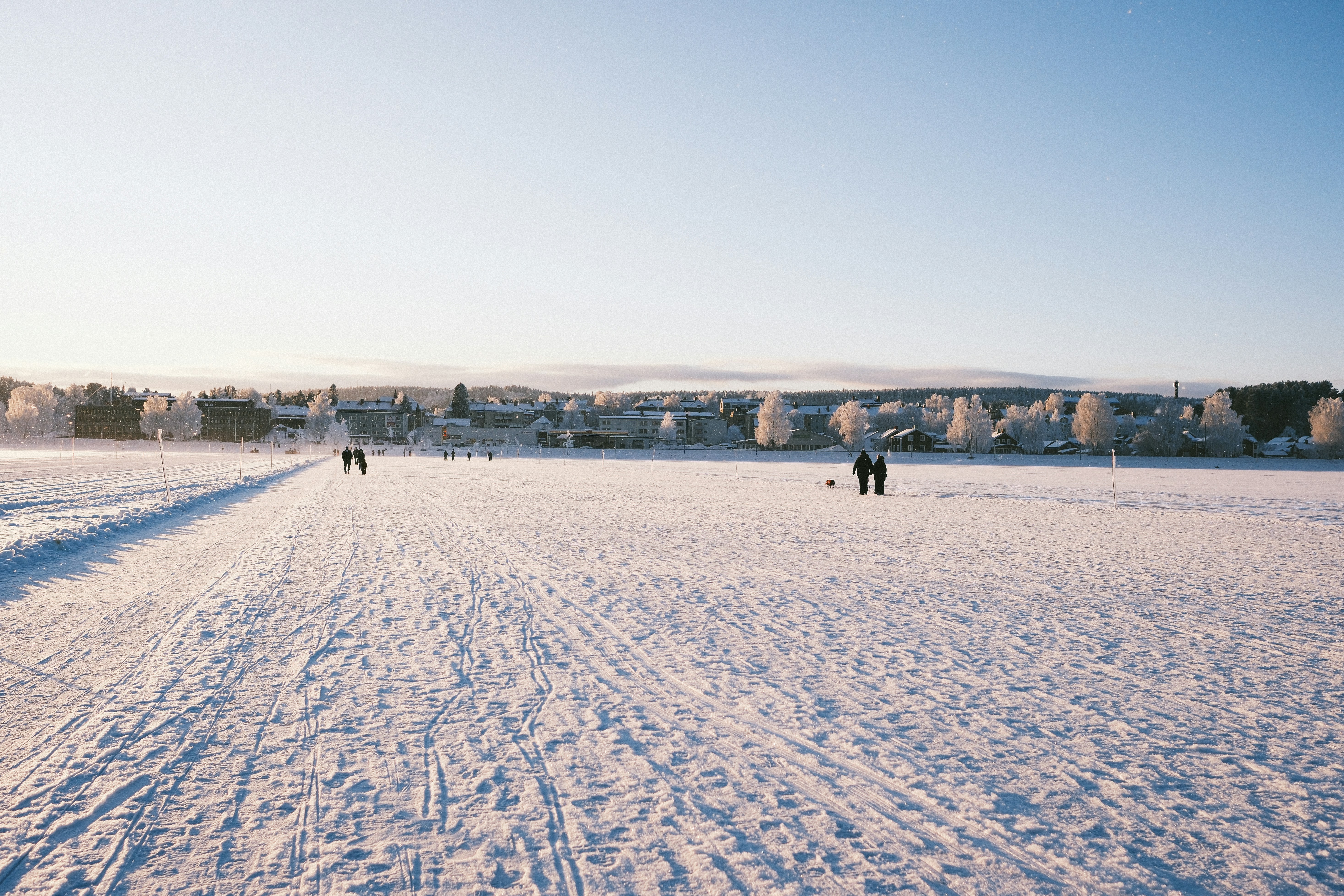 People walking on a snowy field under a clear sky.