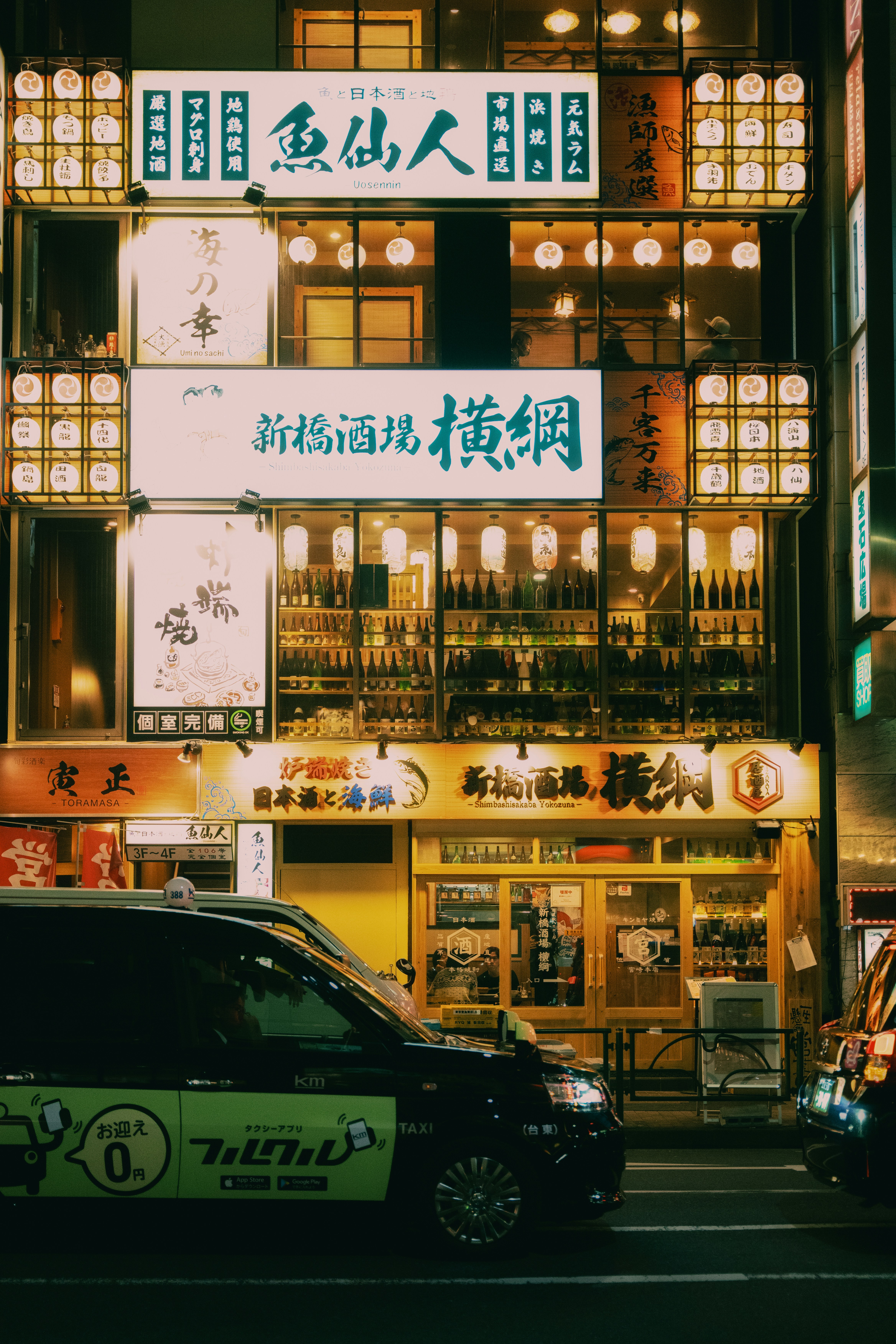 Taxi drives past illuminated japanese restaurant storefront at night