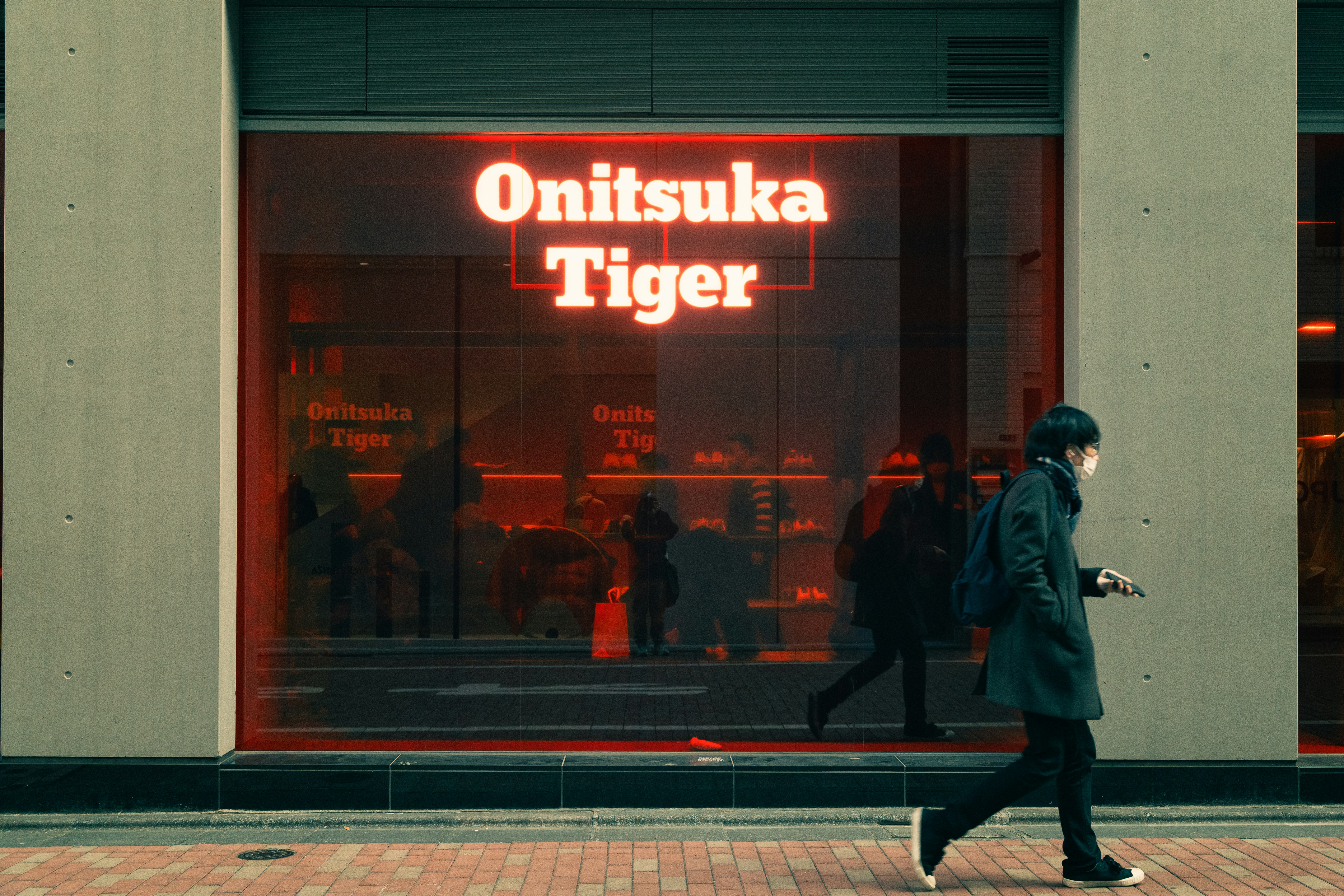 Man walks past a brightly lit onitsuka tiger store