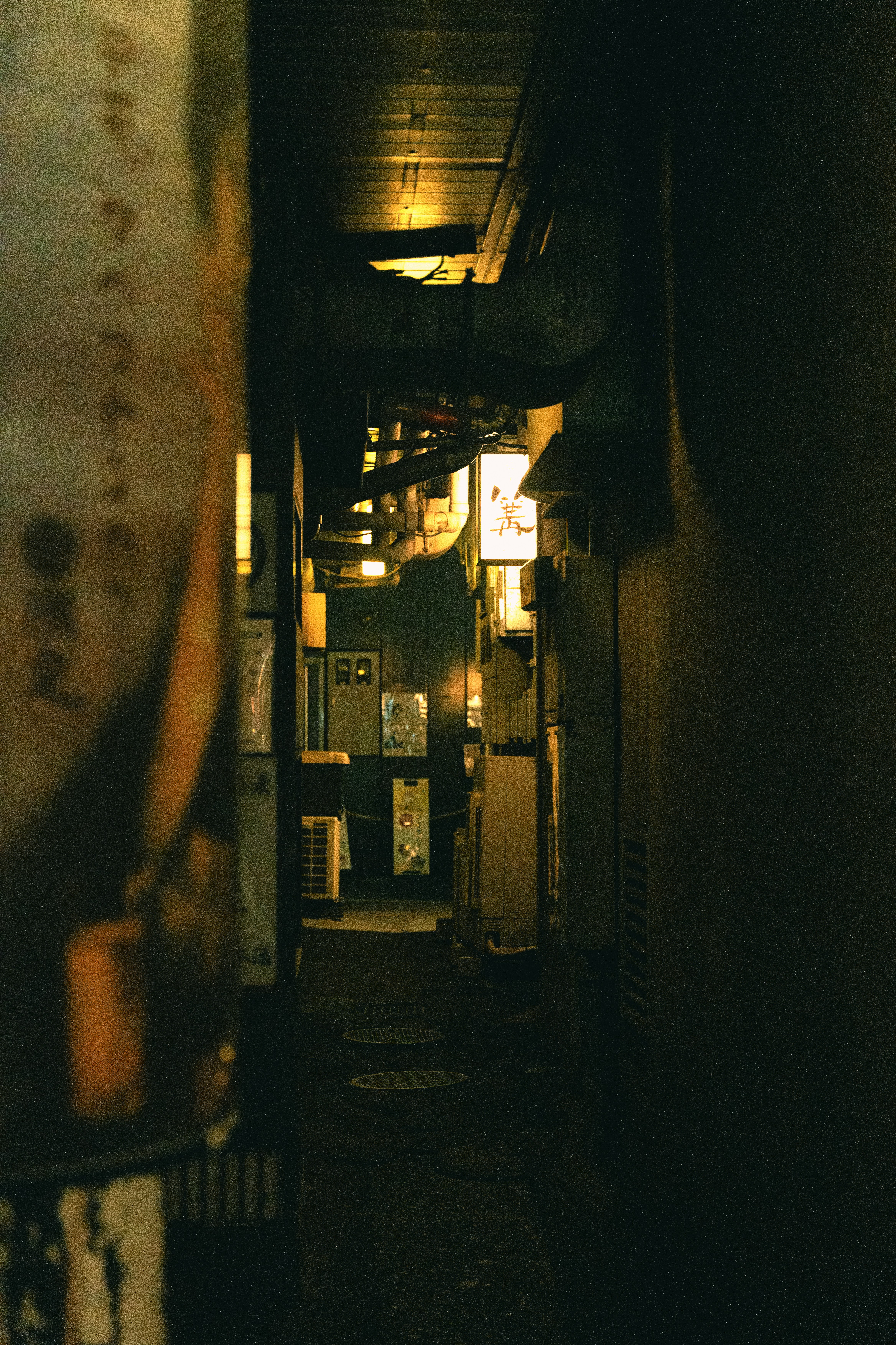 照明付きの看板やパイプがある狭い路地。