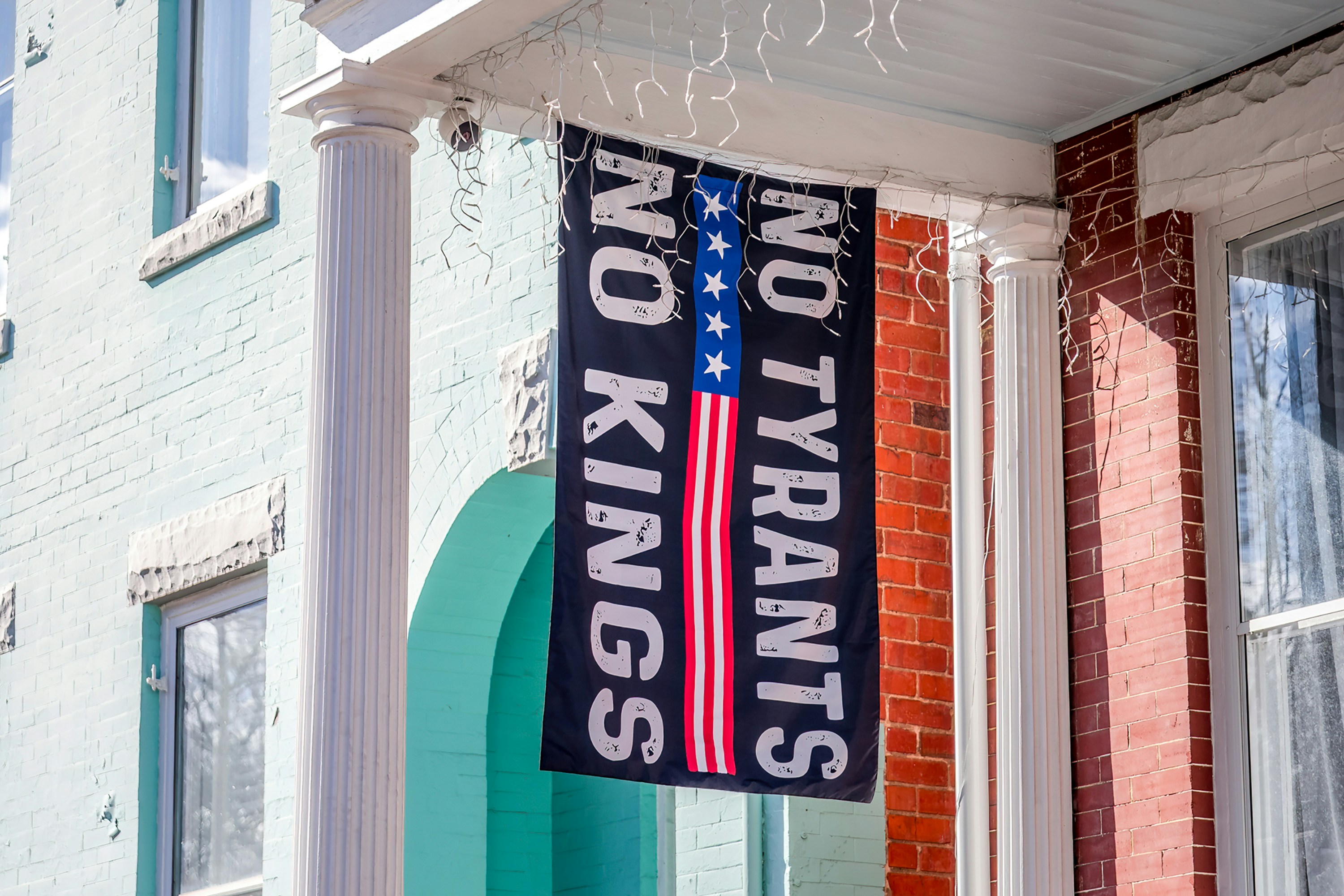 Two flags hang on a porch, one says "no kings".