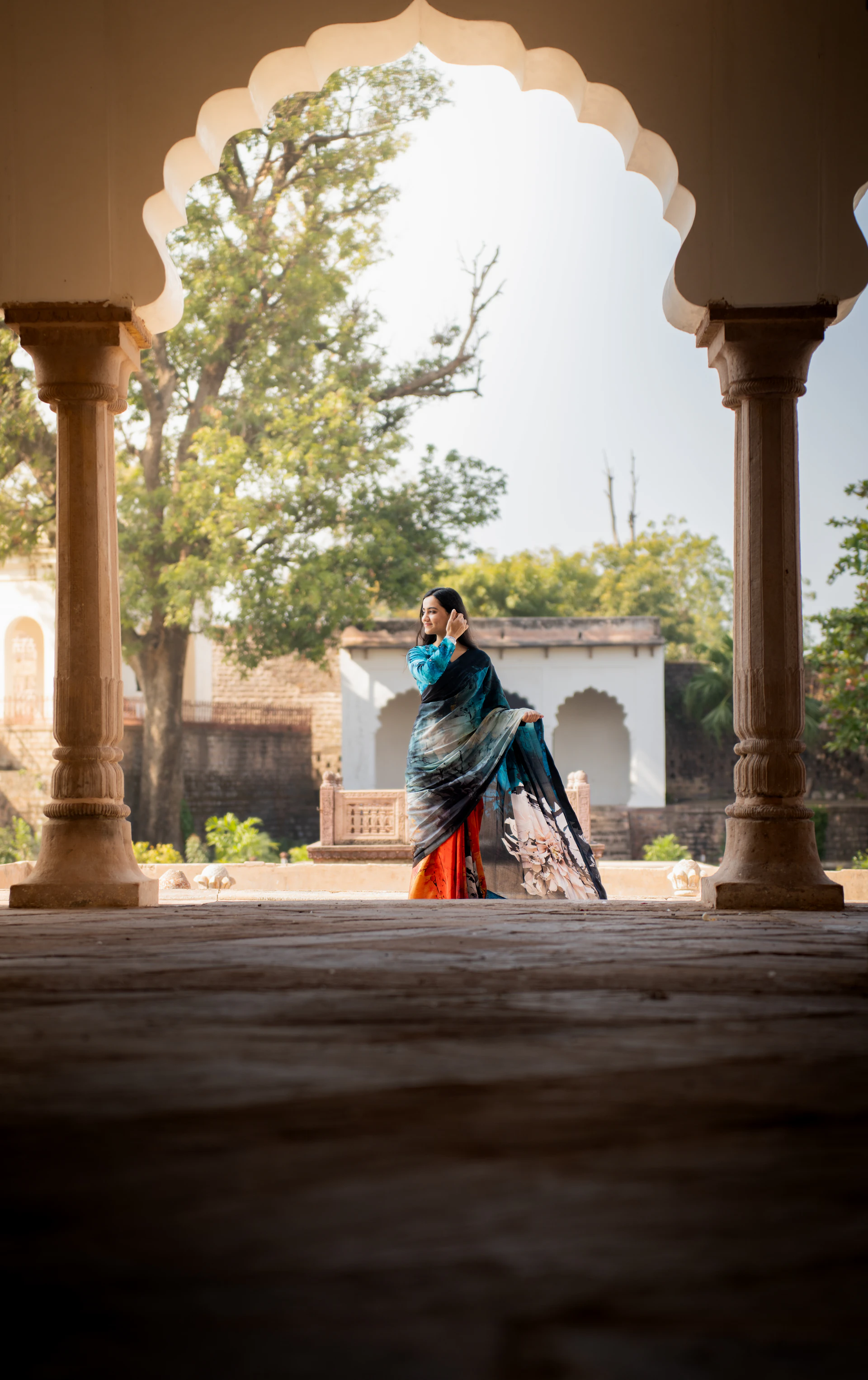 Woman draped in a vibrant traditional Indian silk saree beside heritage architecture