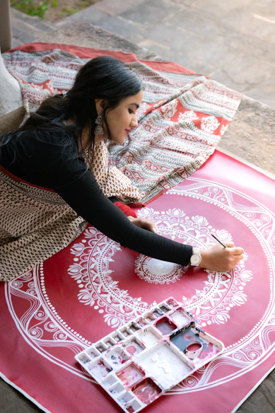 Indian woman in a block-print saree painting white floral art on a red canvas