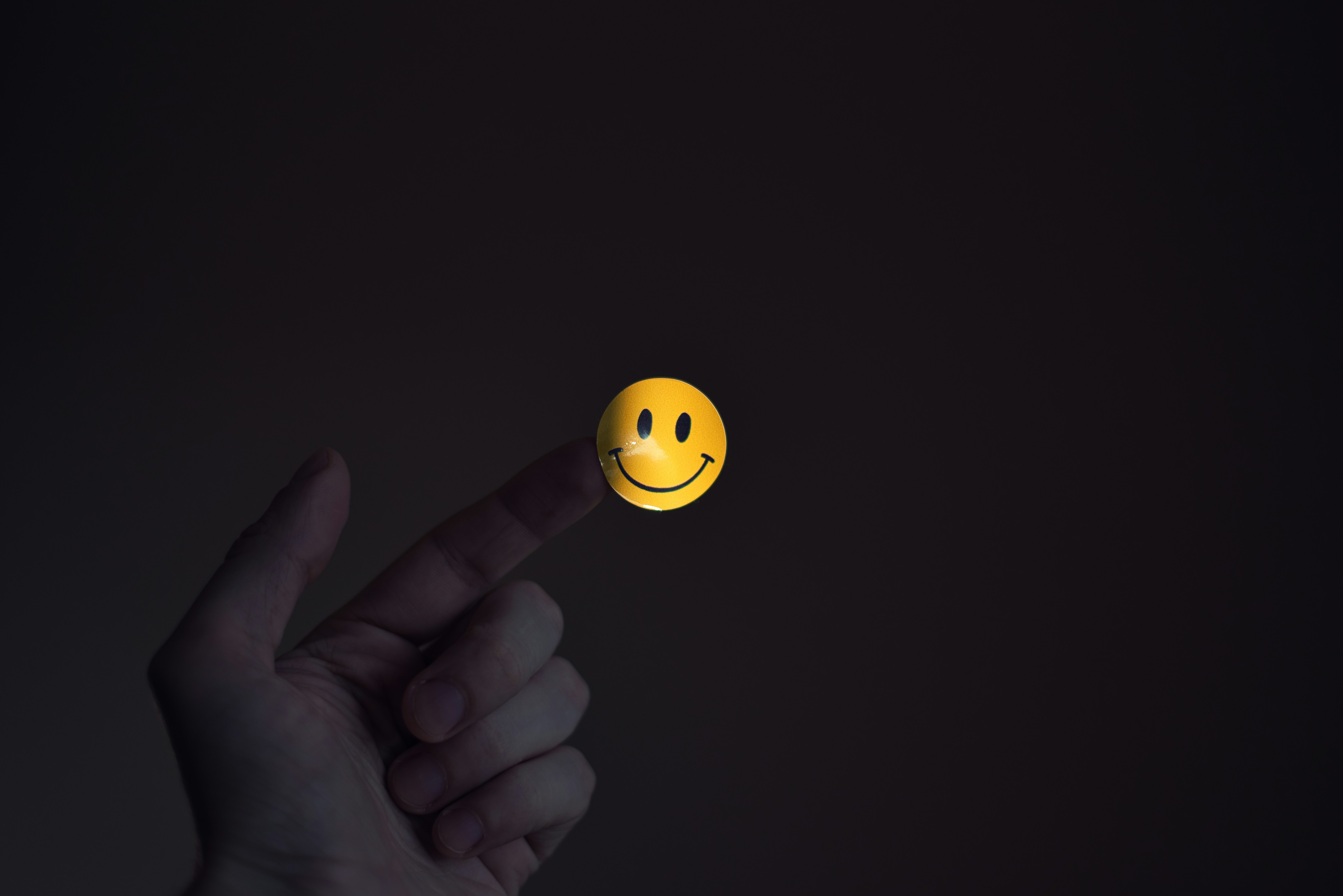Con un dedo sosteniendo una carita sonriente luminosa sobre fondo oscuro