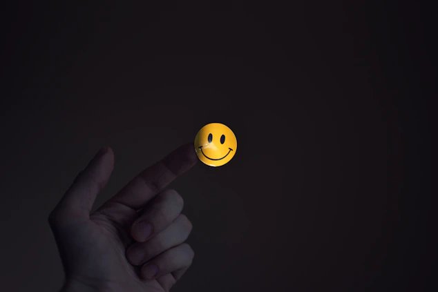 Finger holding a glowing smiley face against dark background