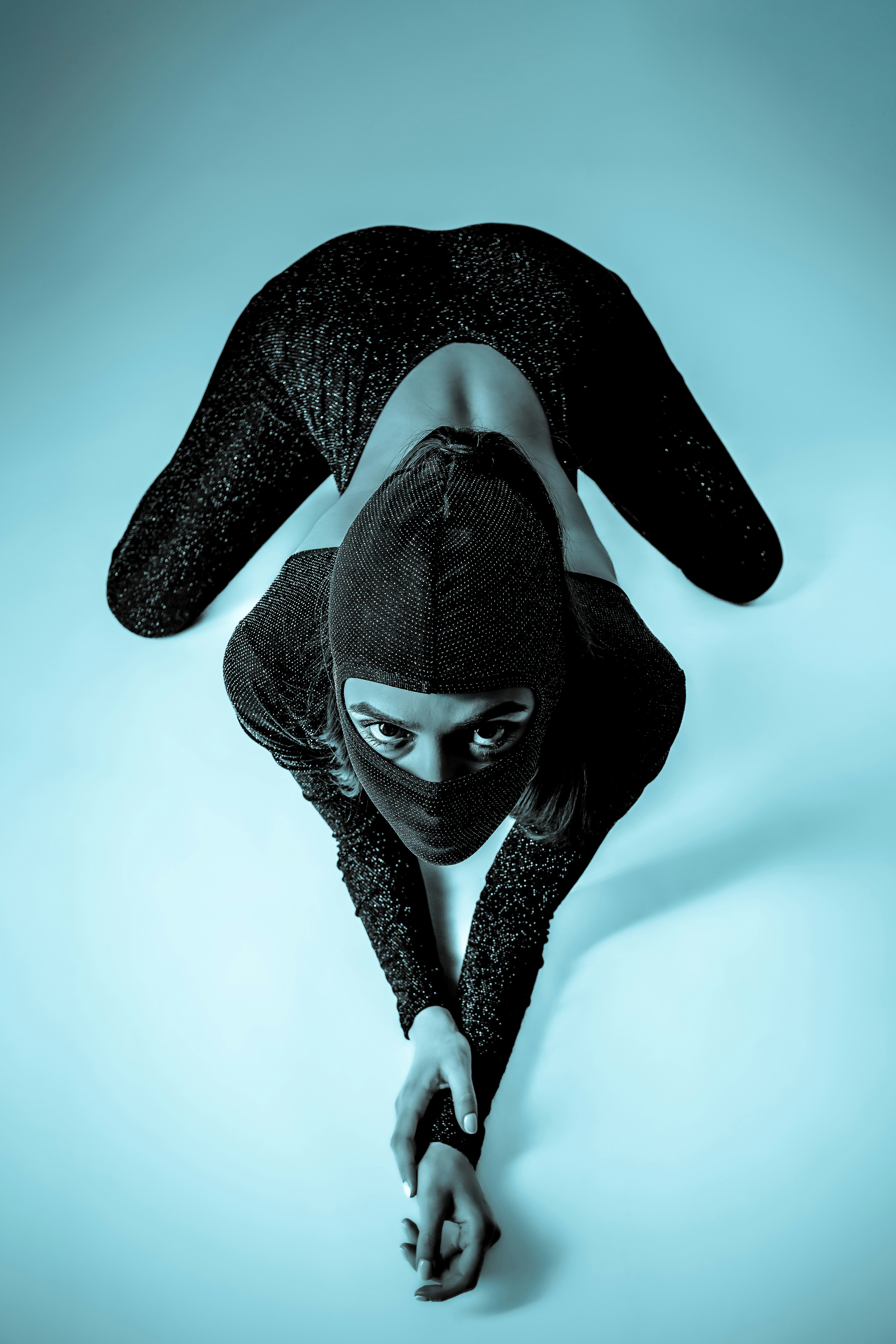 Person in sparkly outfit and balaclava on blue background