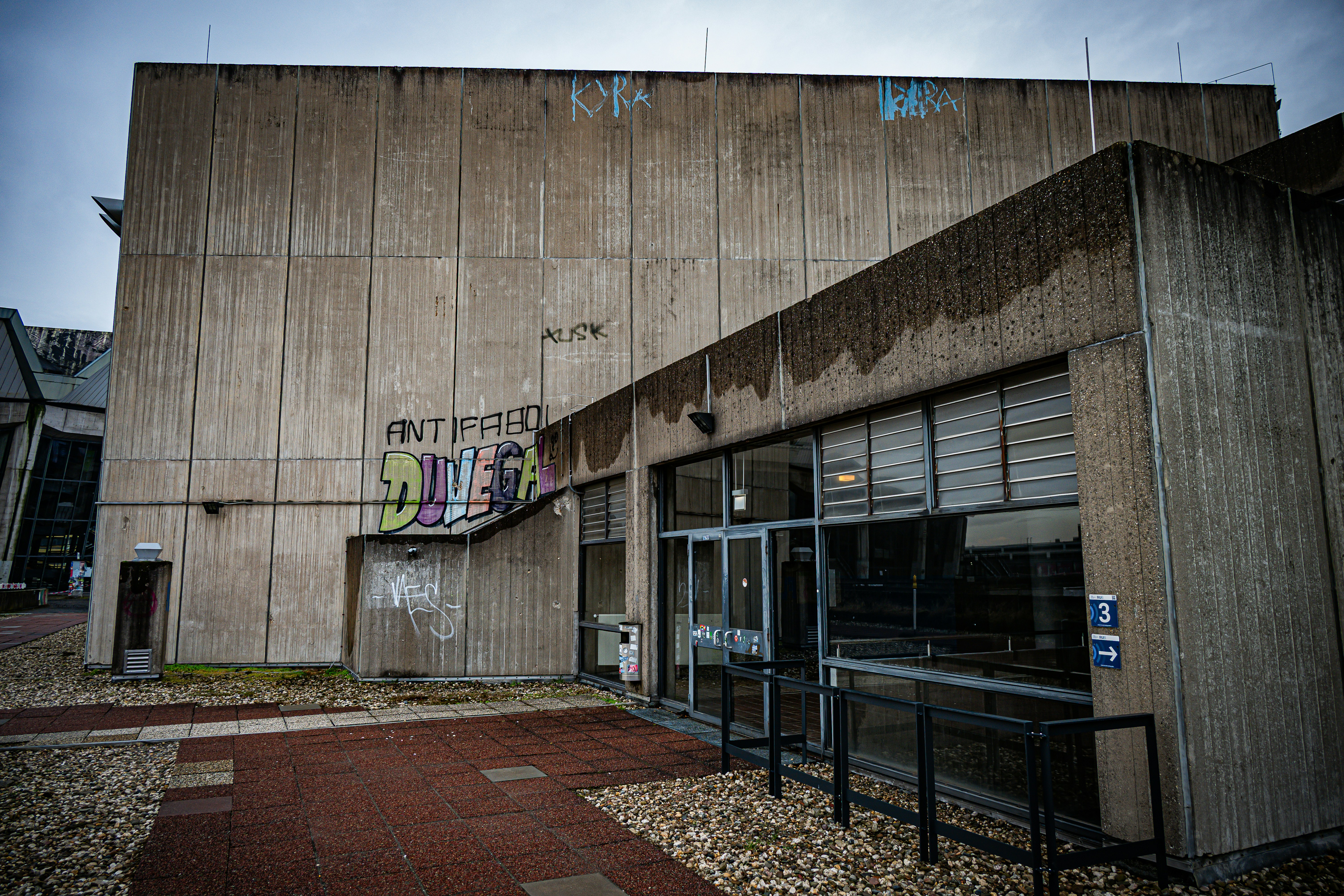 Brutalist concrete building with graffiti and glass entrance.